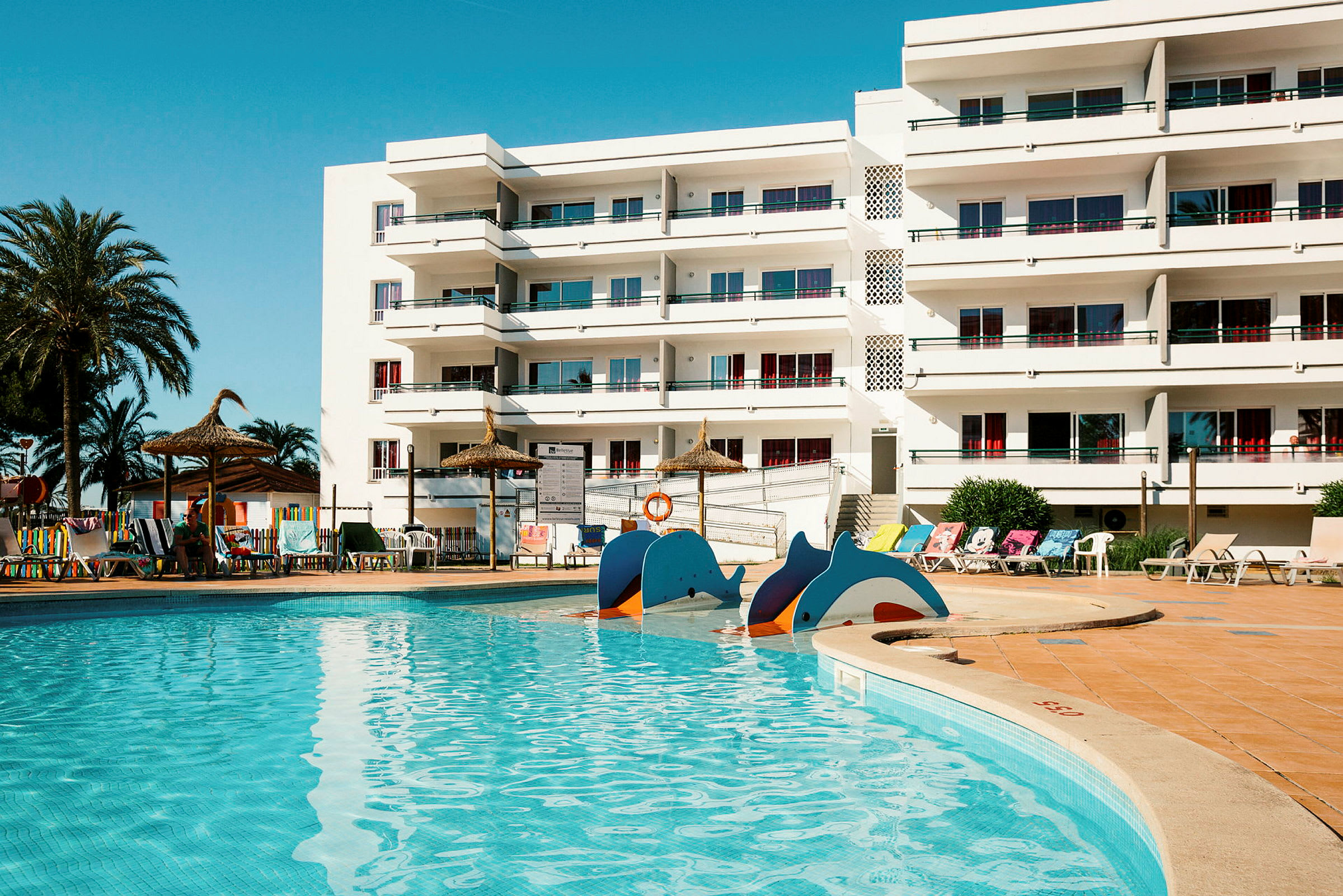 En swimmingpool framför en vit byggnad med balkonger. (AI-genererad text)