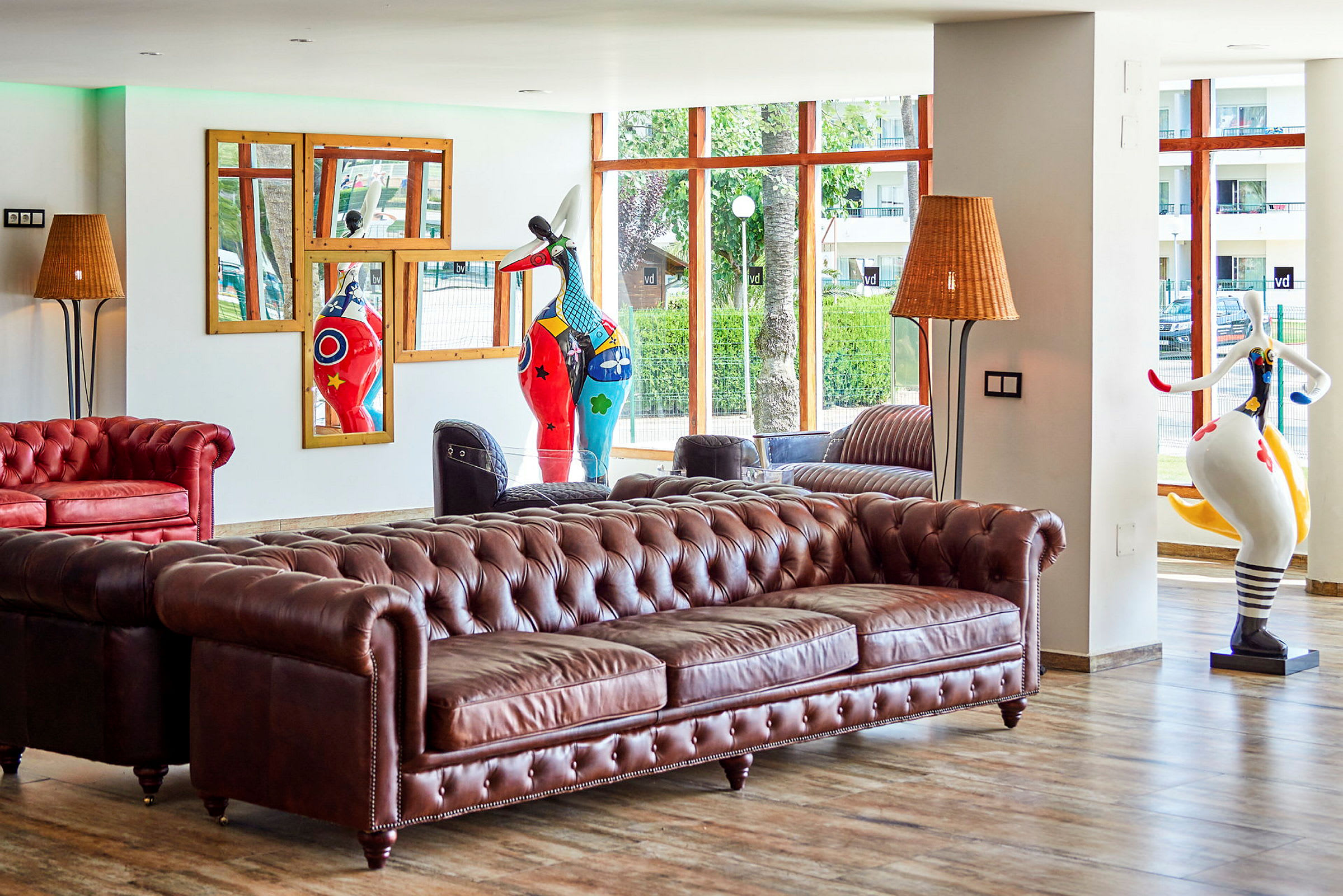 En hotellobby med en brun chesterfield-soffa, dekorativa skulpturer och stora fönster med utsikt. (AI-genererad text)