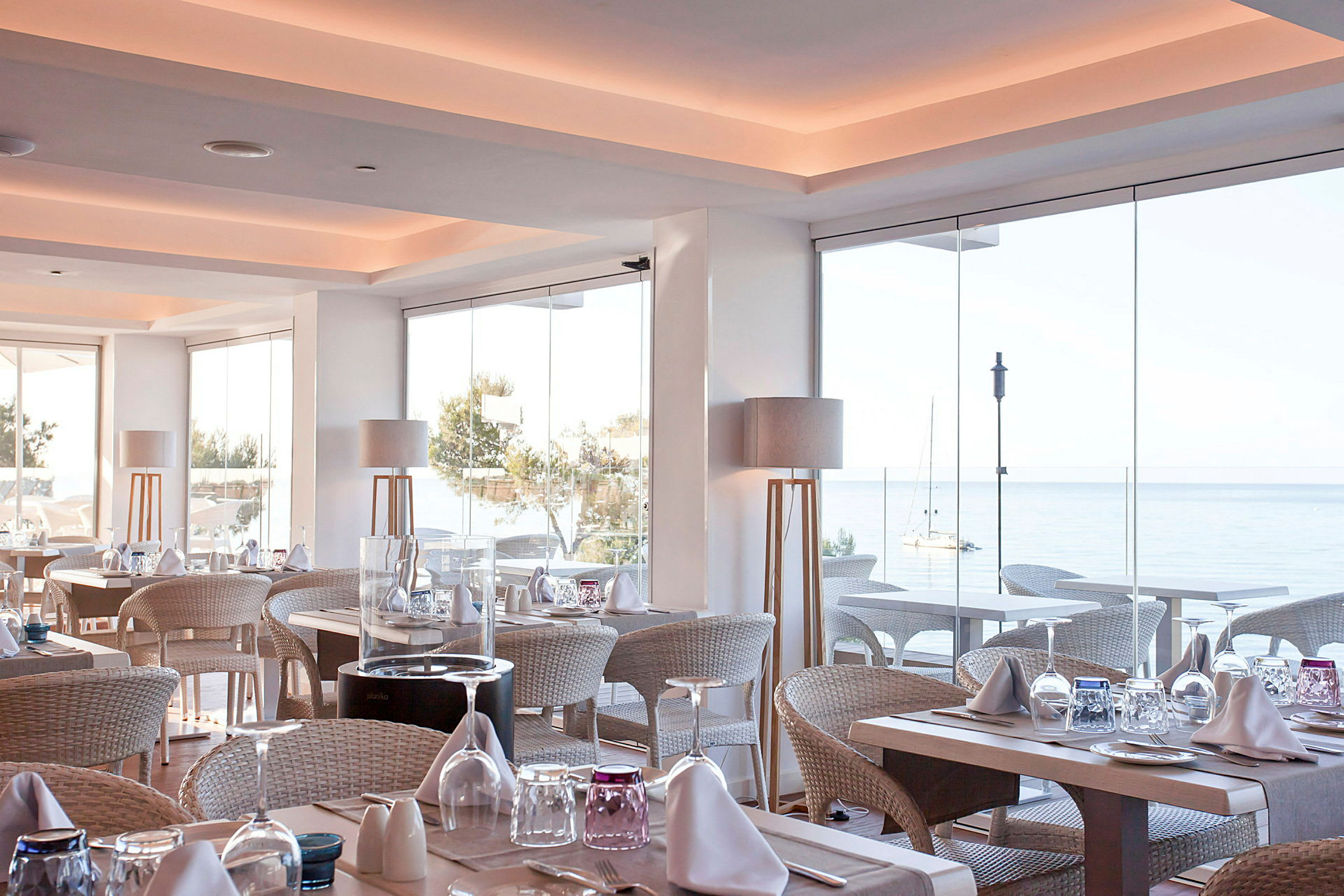 Ljust och modernt inrett restaurangområde med utsikt över havet genom stora glasfönster. (AI-genererad text)