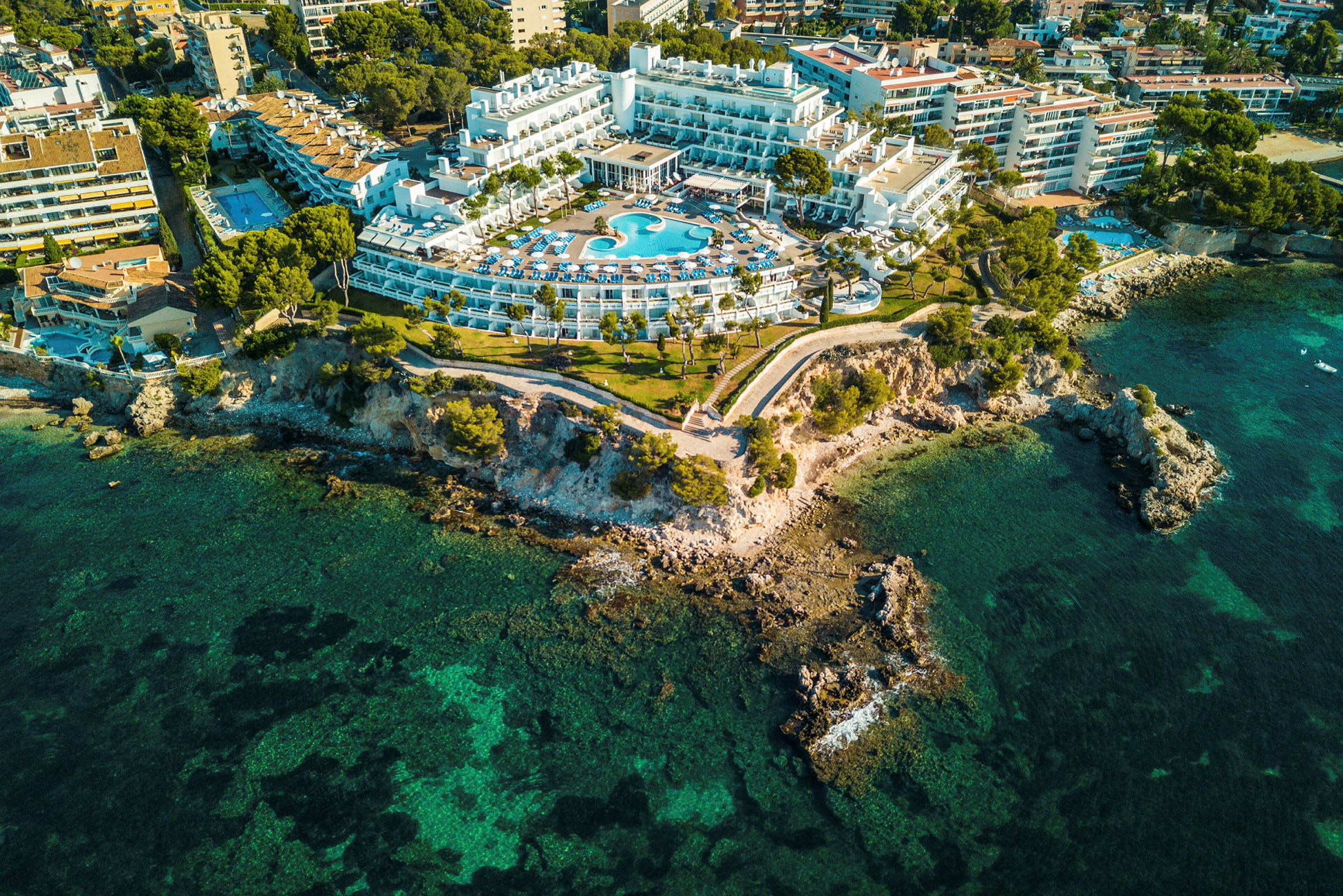 Flygfoto av ett hotell med pool, beläget vid en klippig kust. (AI-genererad text)