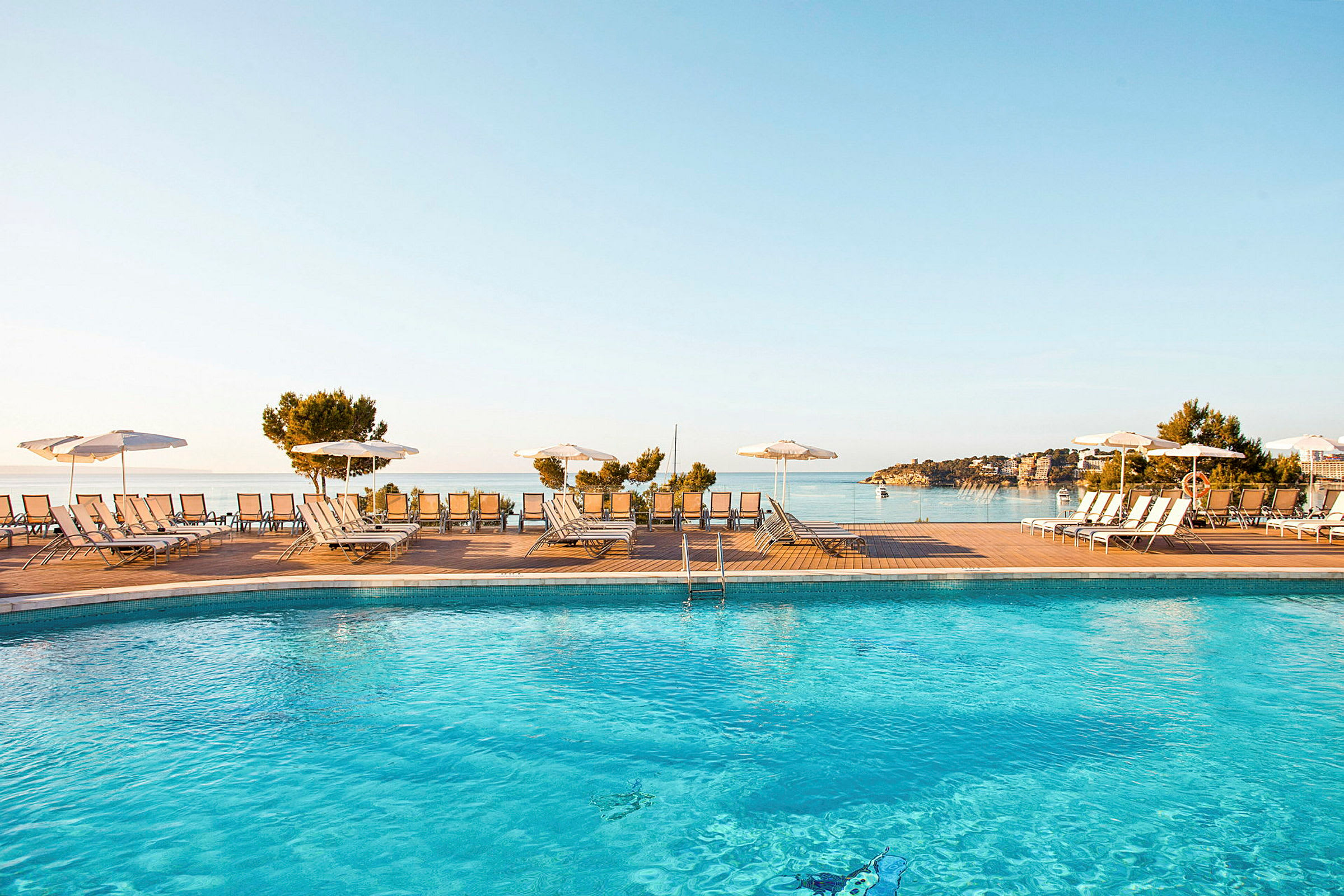 Pool med solstolar och parasoller vid vattnet. (AI-genererad text)