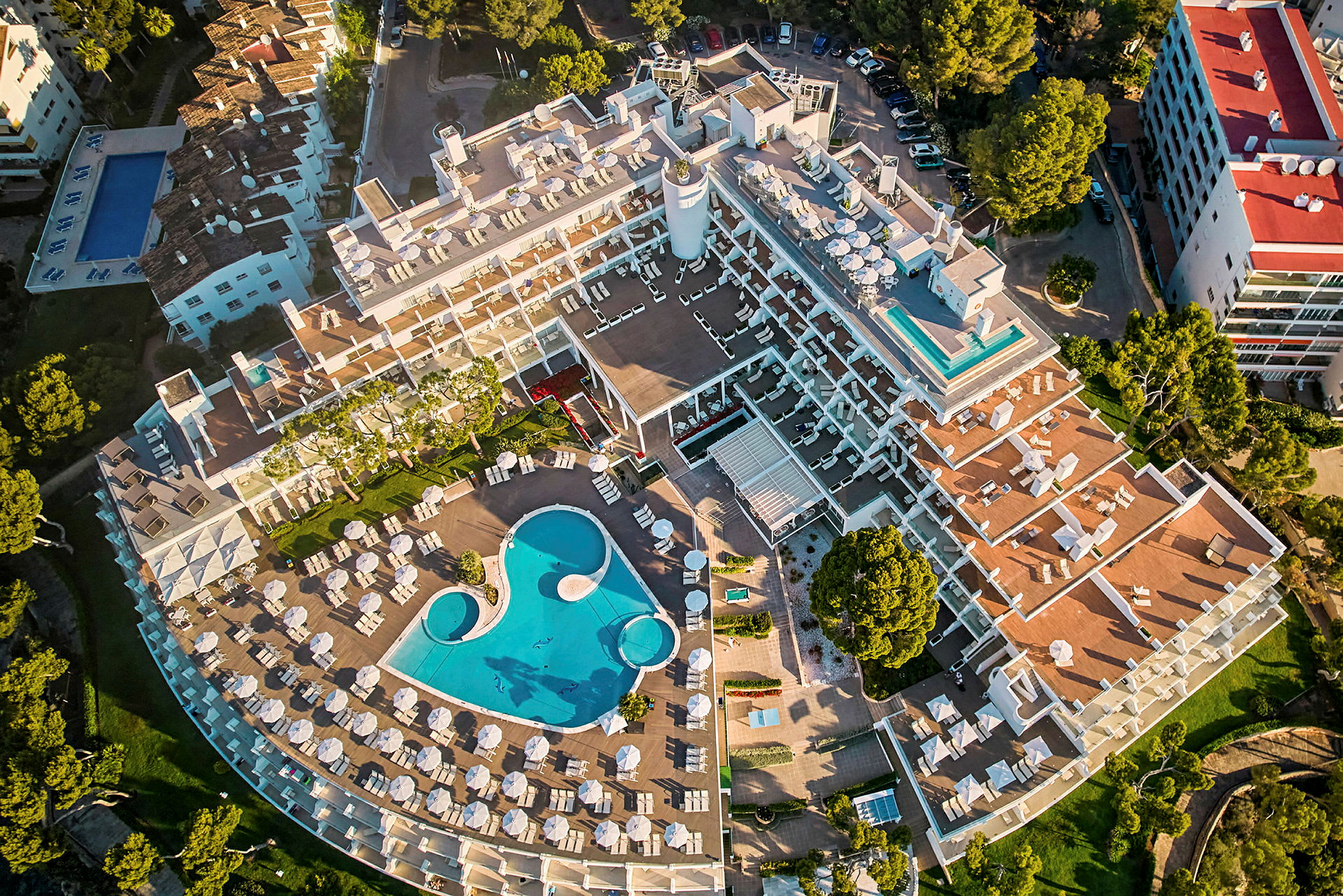 Flygfoto av en hotellbyggnad med utsikt över en pool och solstolsområden. (AI-genererad text)
