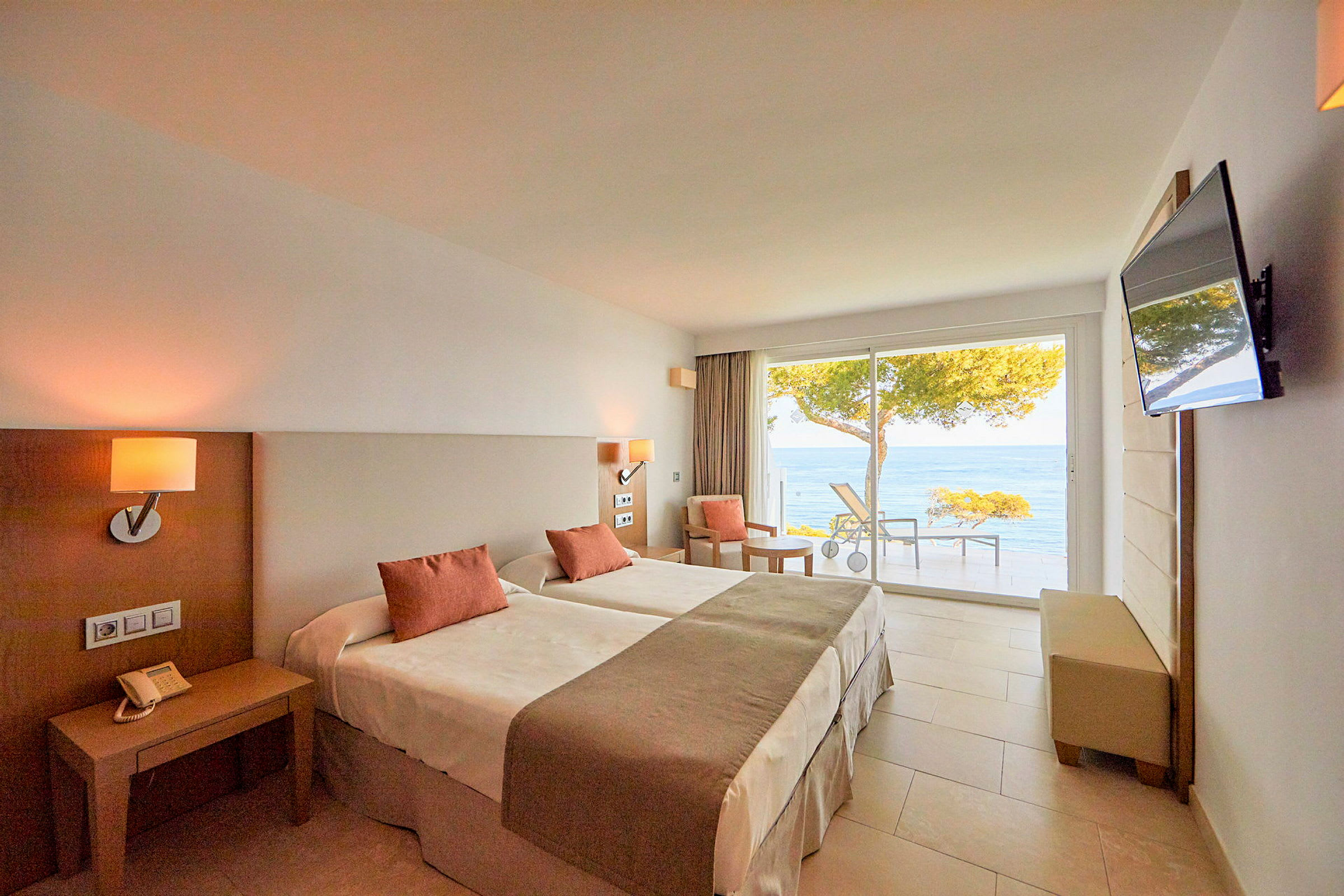 Ett hotellrum med två enkelsängar, en platt-TV på väggen och fönster som vetter mot en havsutsikt. (AI-genererad text)