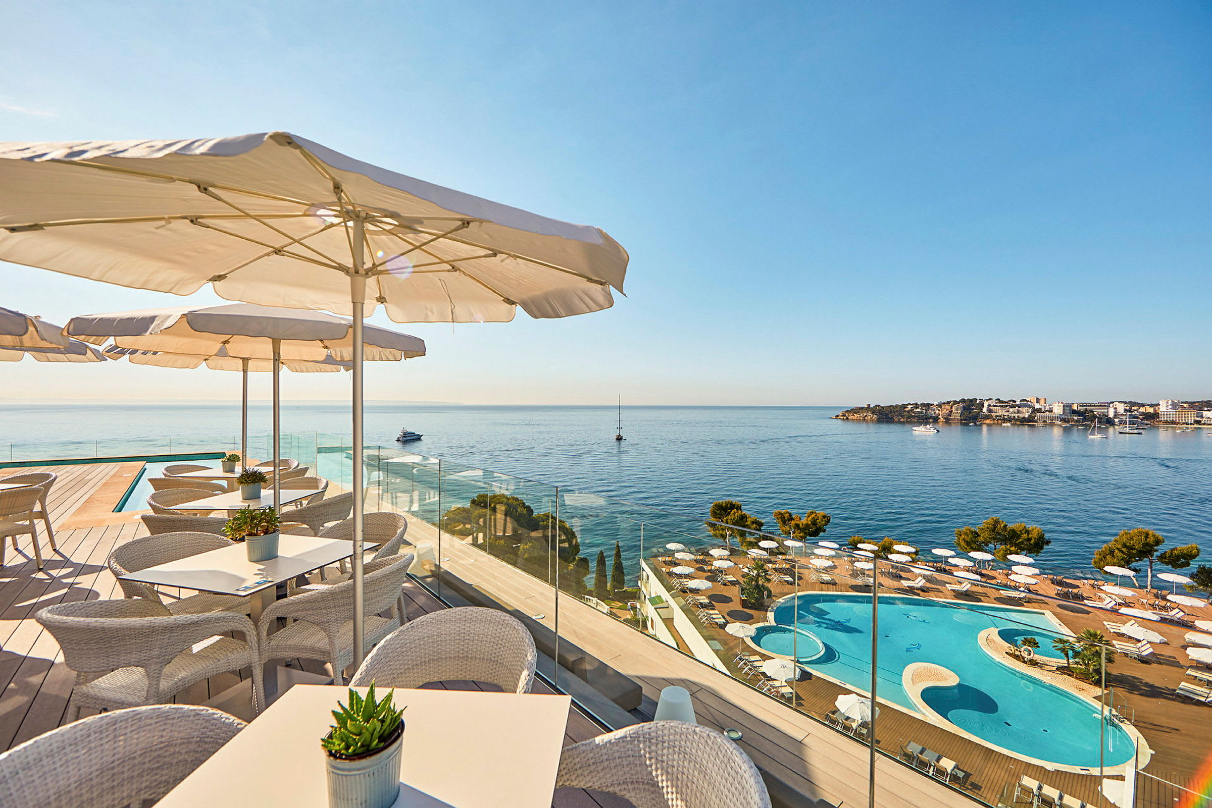 Bild som visar en terrass med sittplatser och parasoller, med utsikt över en pool och havet. (AI-genererad text)