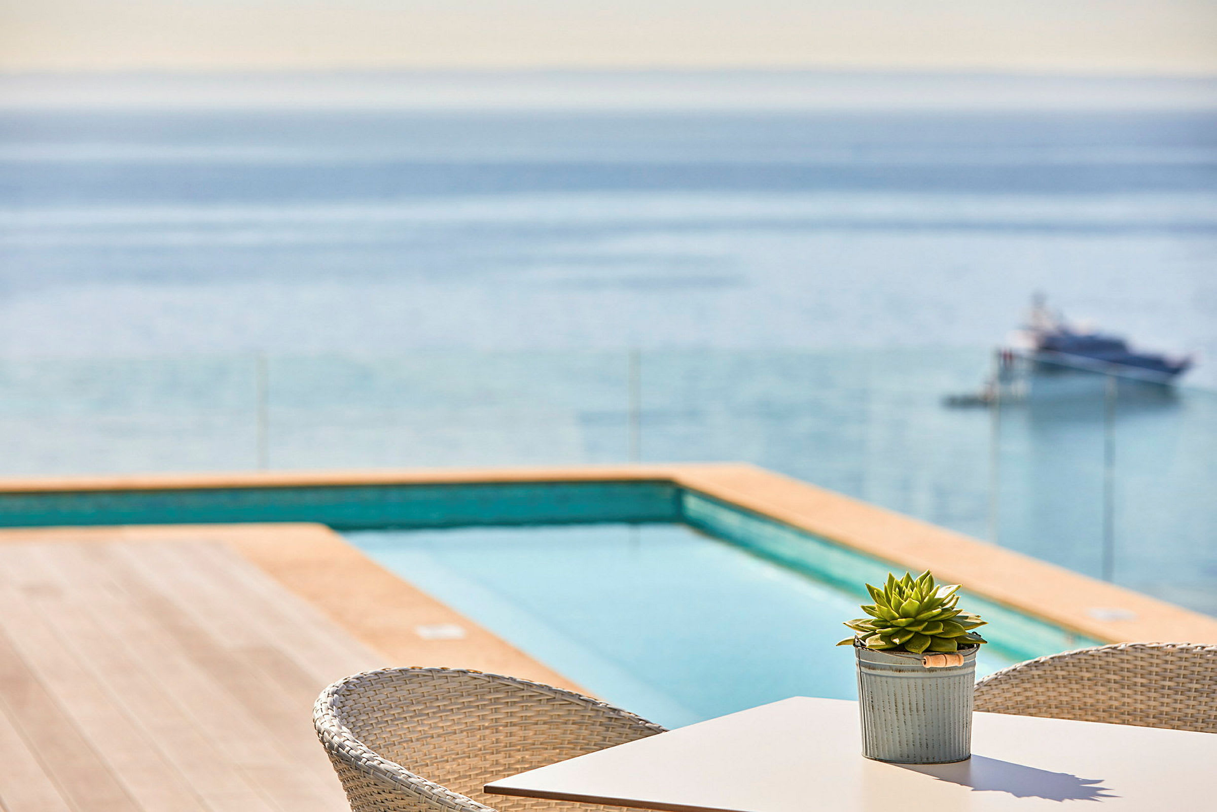 Ett bord med en krukväxt vid en terrass med utsikt över en pool och havet. (AI-genererad text)