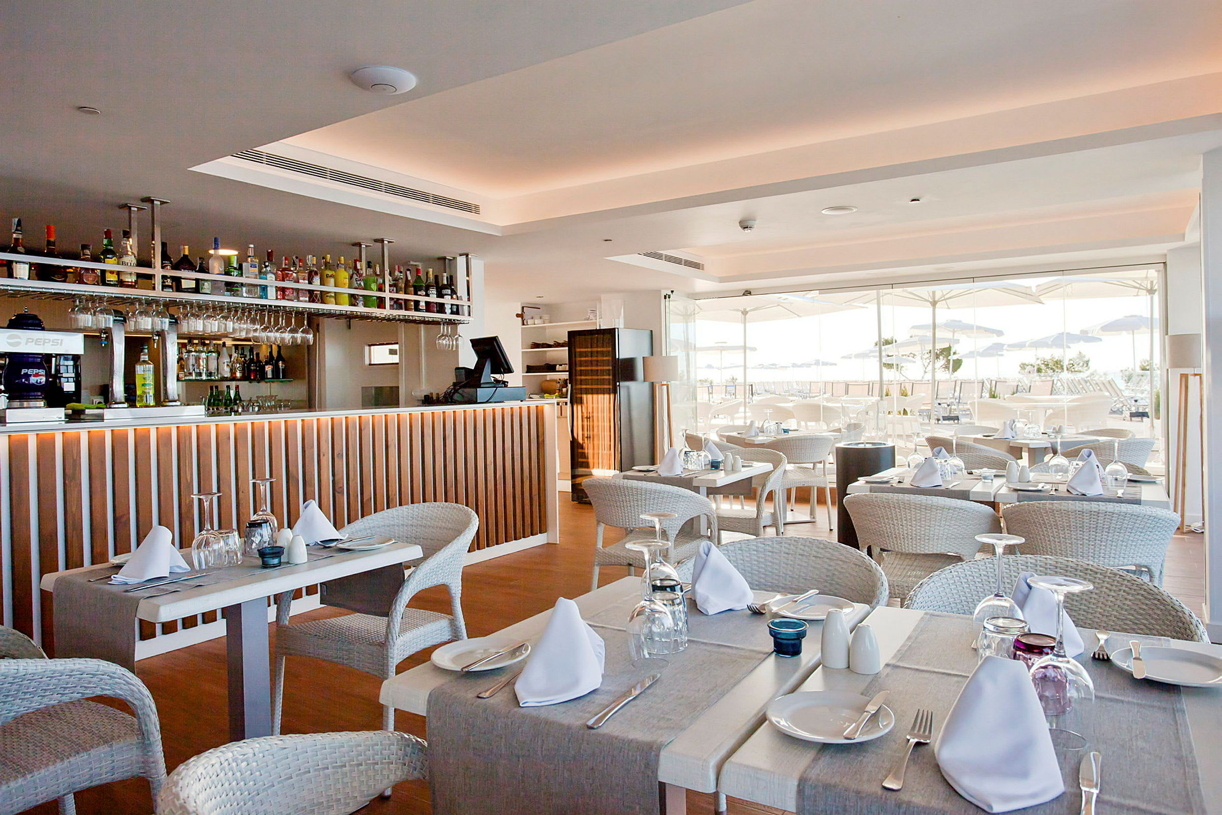 Restaurang med dukade bord och bar. Utsikt över utomhusterrass med parasoll. (AI-genererad text)