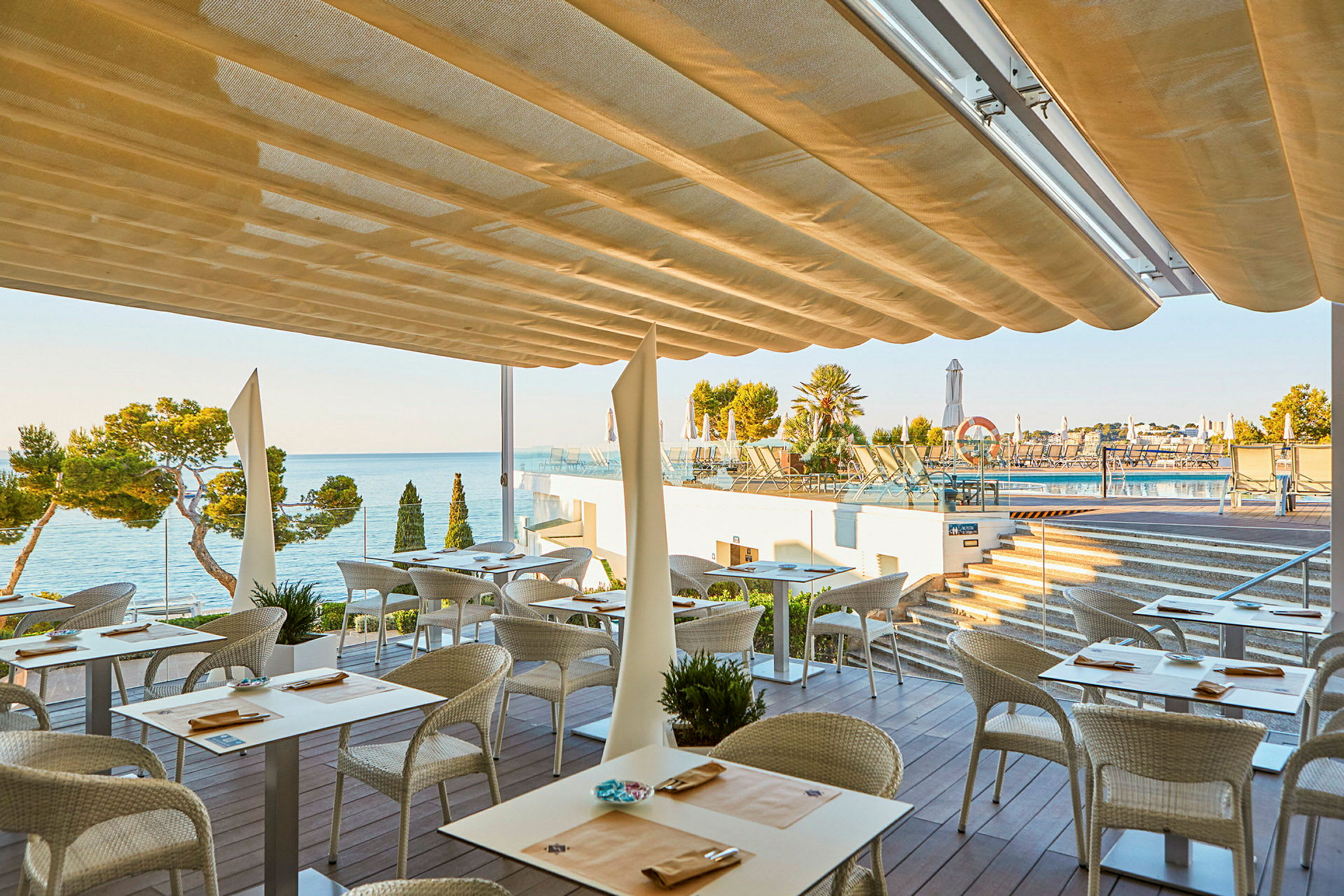 En restaurang med uteservering under en markis med utsikt över havet och en pool. (AI-genererad text)