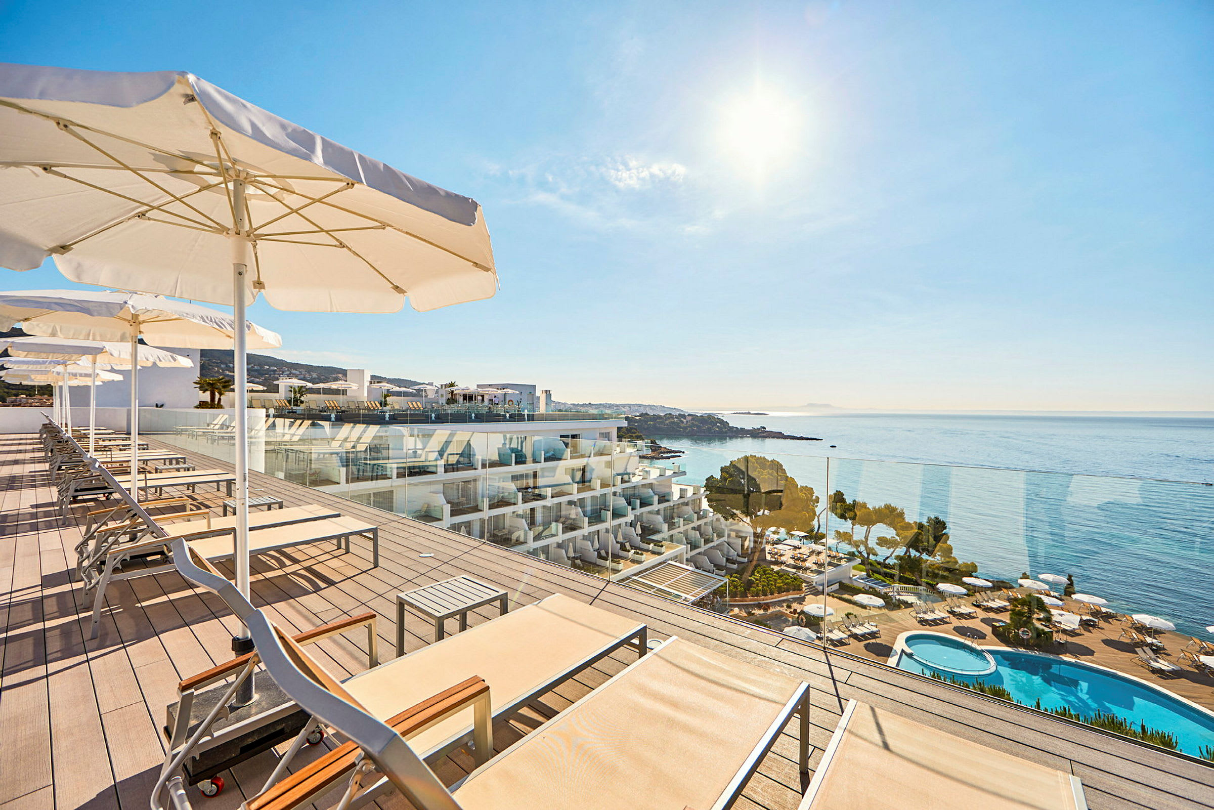 Solstolar och parasoller på en terrass med utsikt över havet och en swimmingpool. (AI-genererad text)