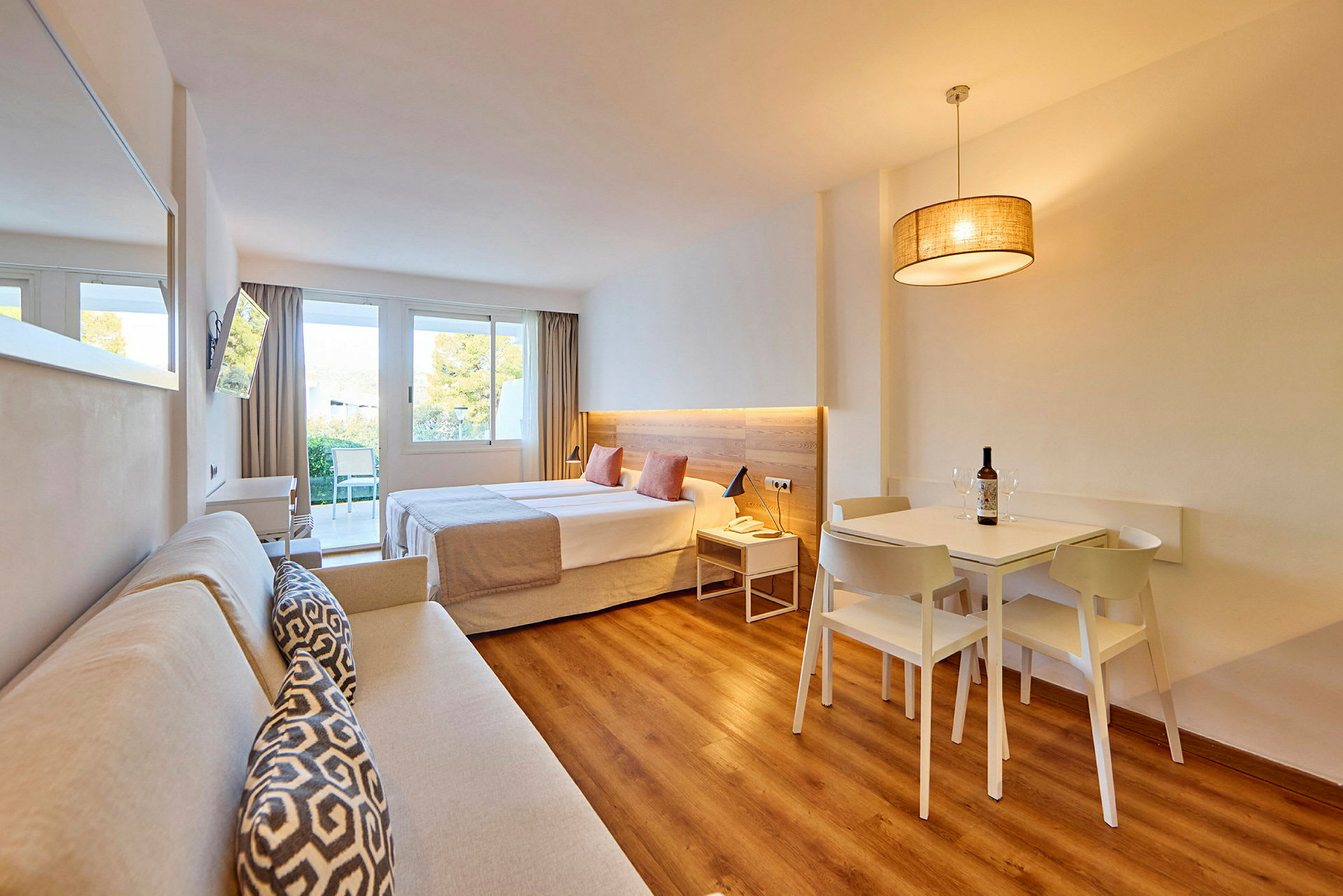 Ett modernt hotellrum med en dubbelsäng, soffa, matbord och stora fönster som släpper in naturligt ljus. (AI-genererad text)