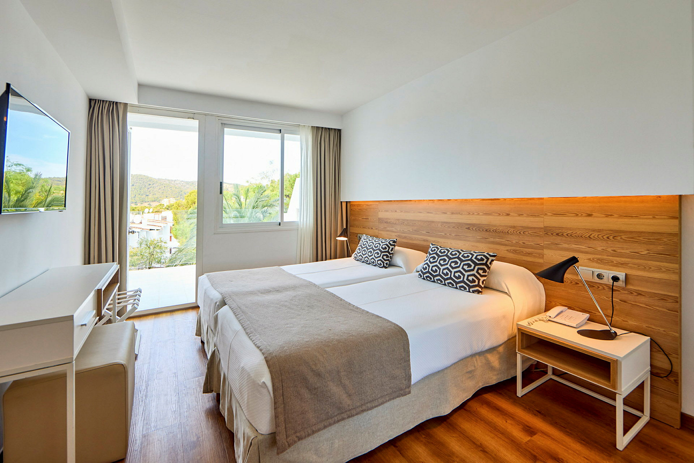 Hotellrum med två enkelsängar, en väggpanel i trä och ett fönster med utsikt. (AI-genererad text)