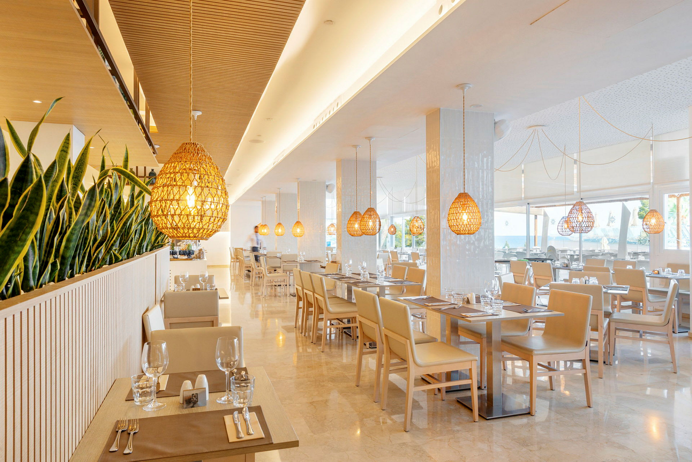 En modern och ljus restaurang med växter som avgränsning och hängande lampor i trädesign. (AI-genererad text)