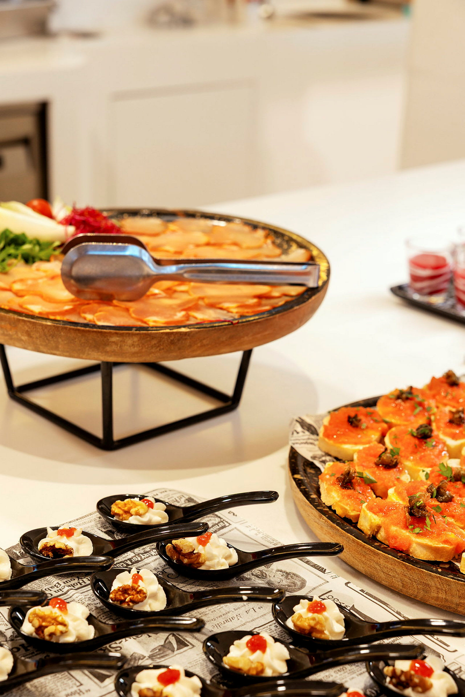 En buffé med olika rätter, inklusive små portioner serverade i svarta skedar, en tallrik med orange färgad mat och dekorerade brödbitar. (AI-genererad text)