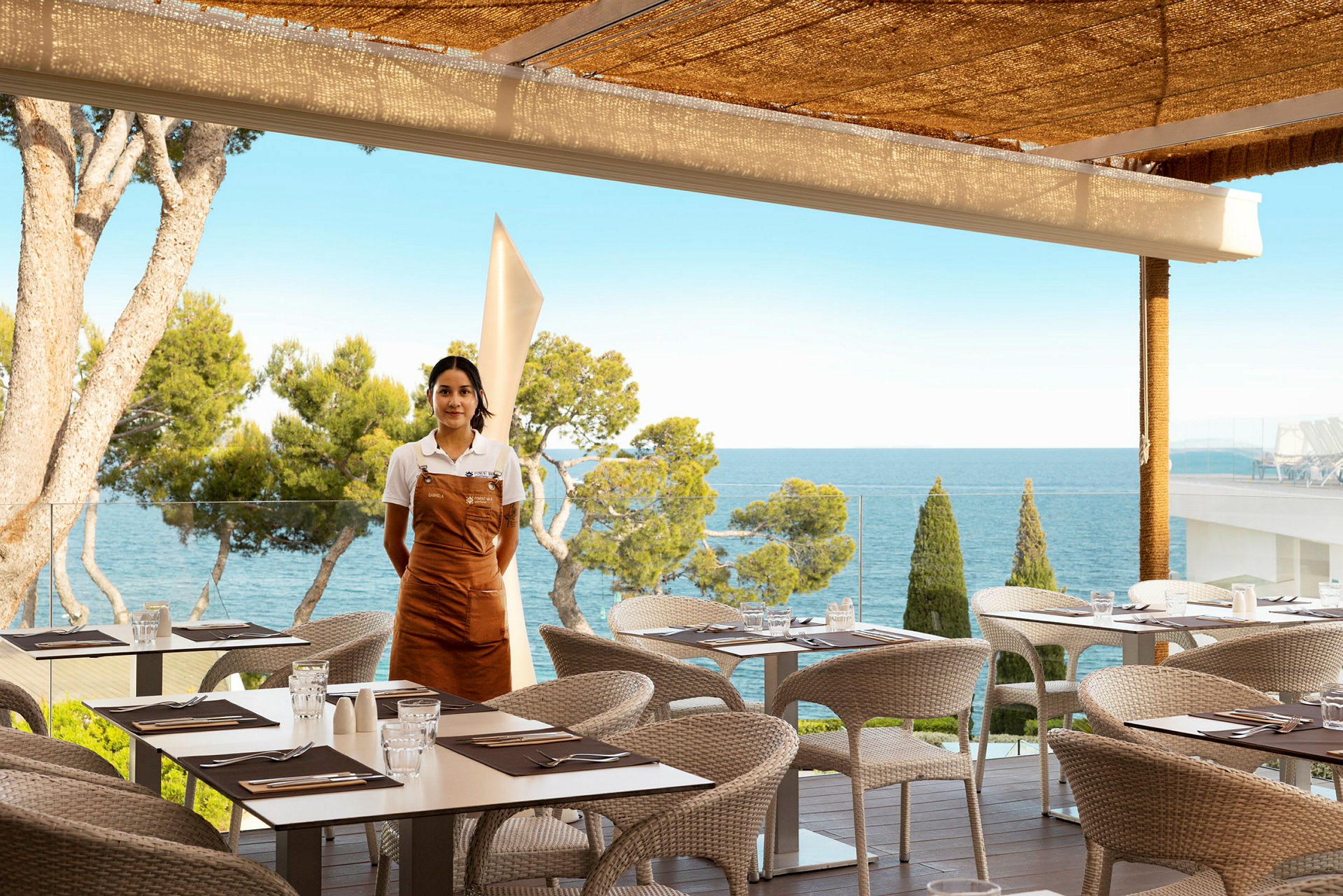 Restaurang med uteservering och havsutsikt, en servitör står vid sidan. (AI-genererad text)