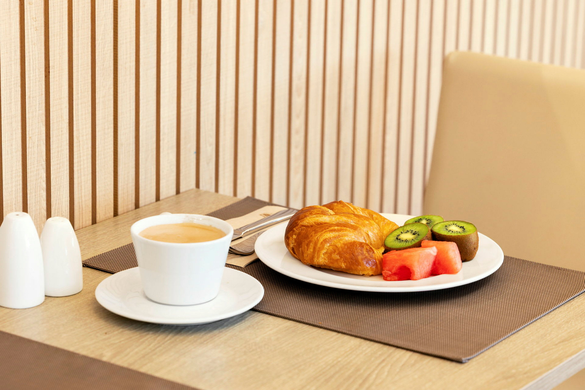 En frukost med kaffe, croissant och färsk fruktservering på bordet. (AI-genererad text)
