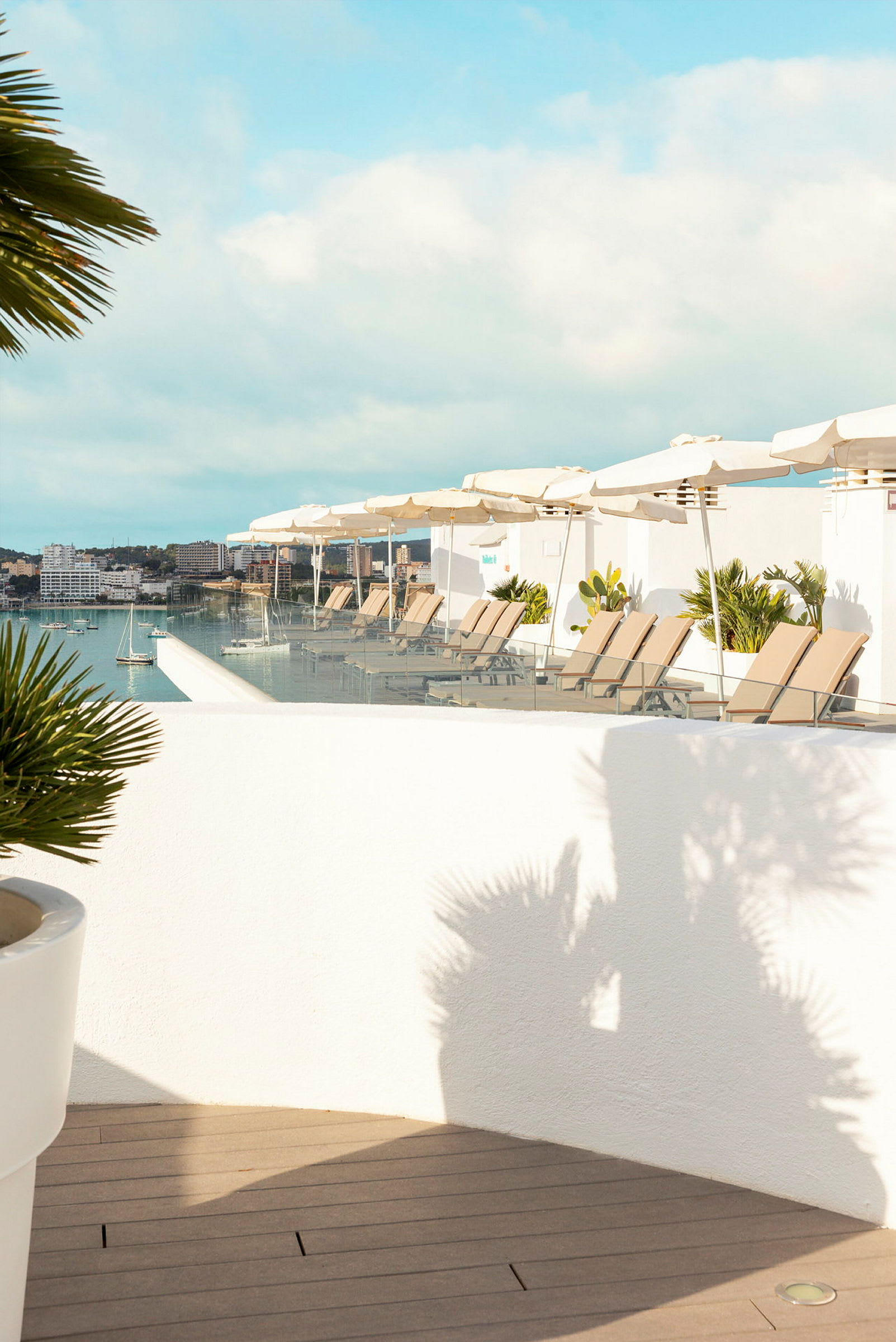 En terrass med solstolar och parasoller vid en infinitypool med utsikt över en hamn. (AI-genererad text)