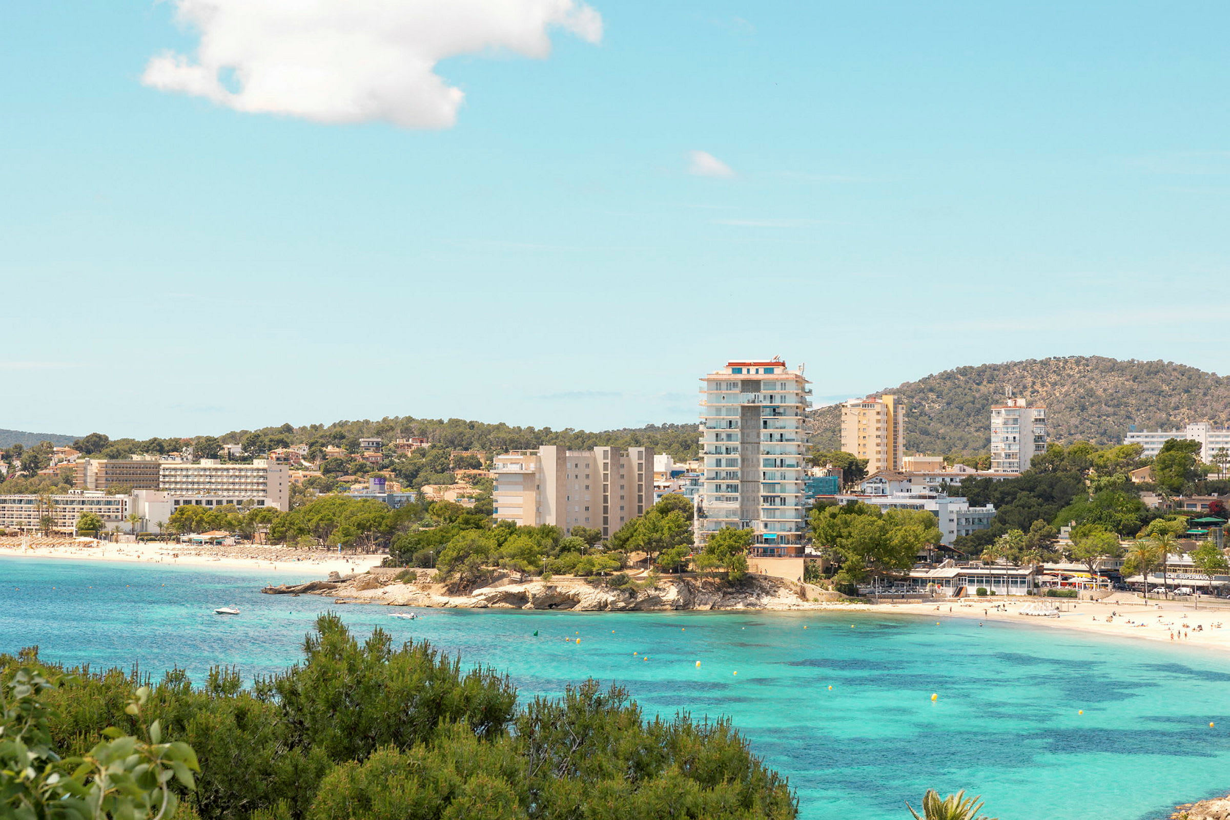 En kuststad med hotell byggnader vid en strand och klart turkost vatten. (AI-genererad text)