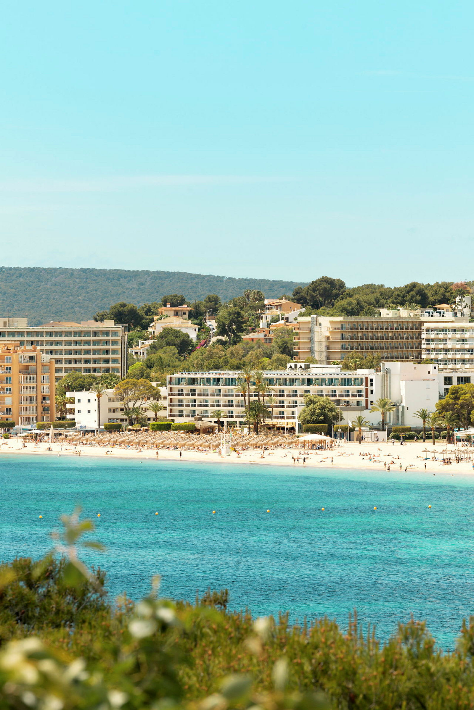En strand med klart blått vatten och hotellbyggnader i bakgrunden. (AI-genererad text)