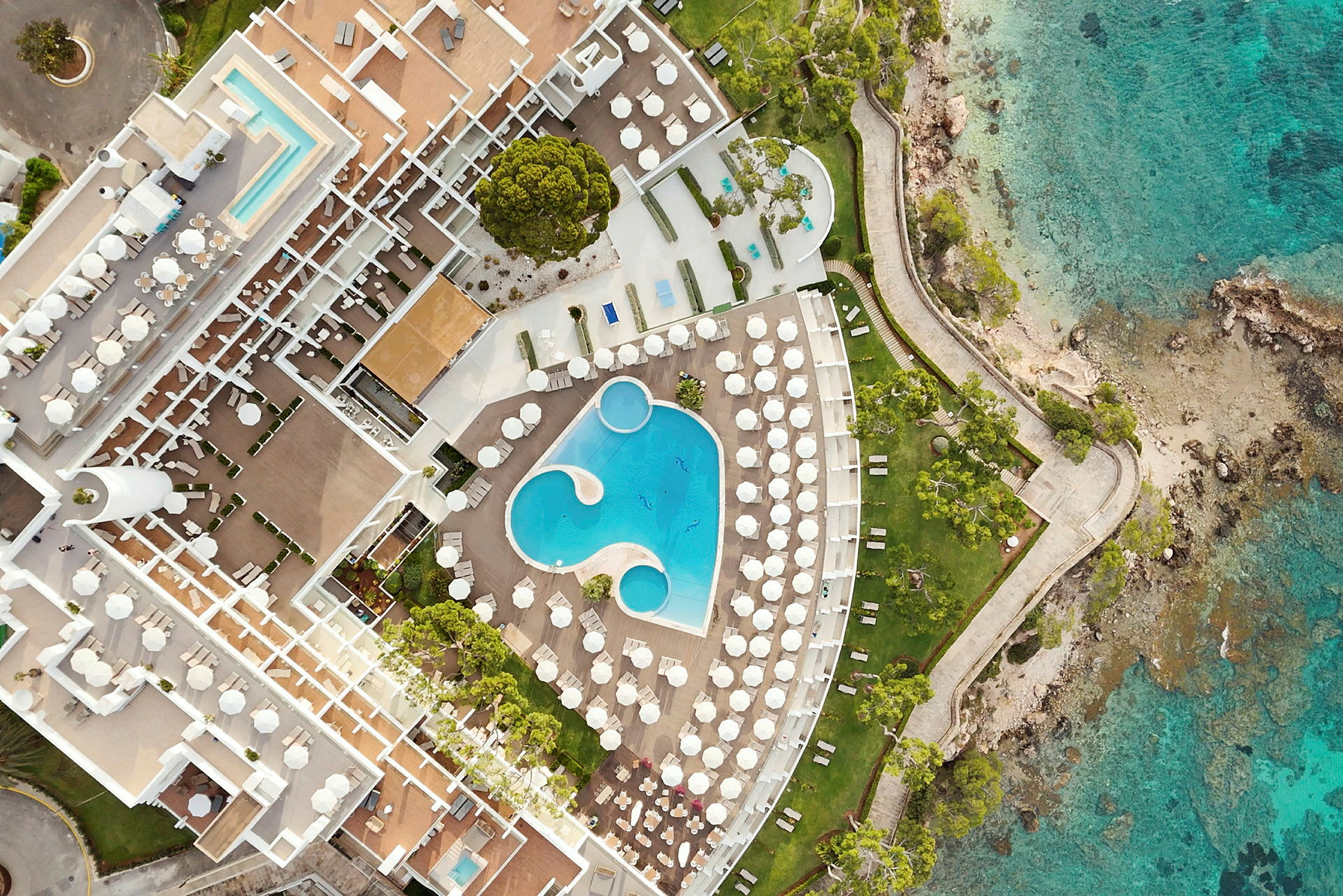 Flygfoto av ett hotellområde med pooler, solstolar och strandlinje. (AI-genererad text)