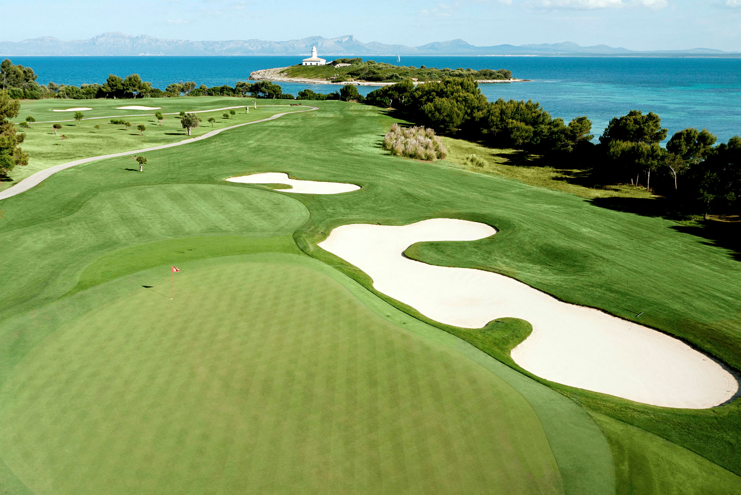 En golfbana med en green och sandbunkrar, omgiven av grönska och havet i bakgrunden. (AI-genererad text)