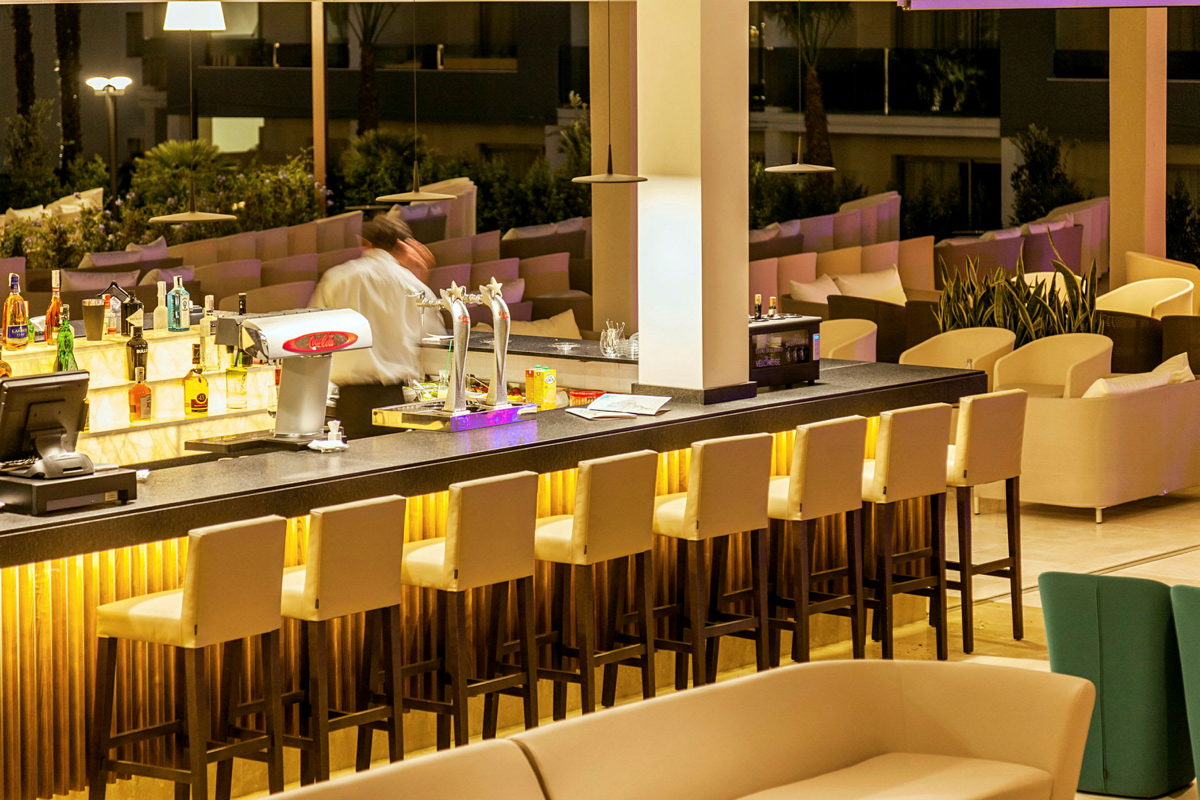 En modern bar med hög ryggstolar, en bartender och dekorativ belysning. (AI-genererad text)