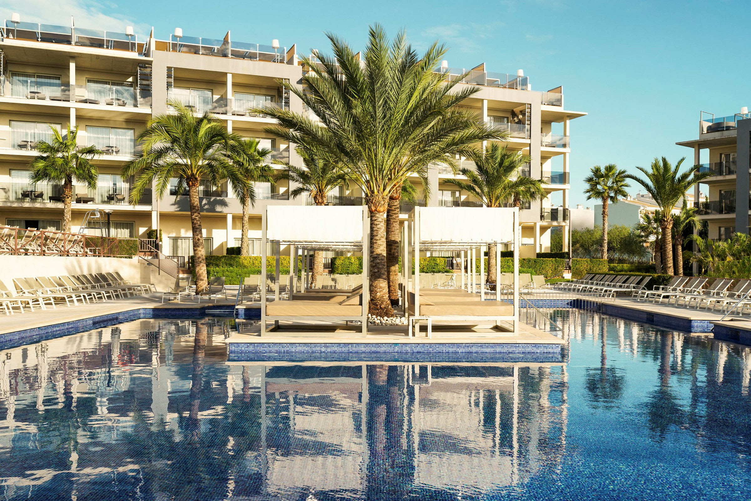 Bild av hotellpool med solstolar, palmer och byggnader i bakgrunden. (AI-genererad text)