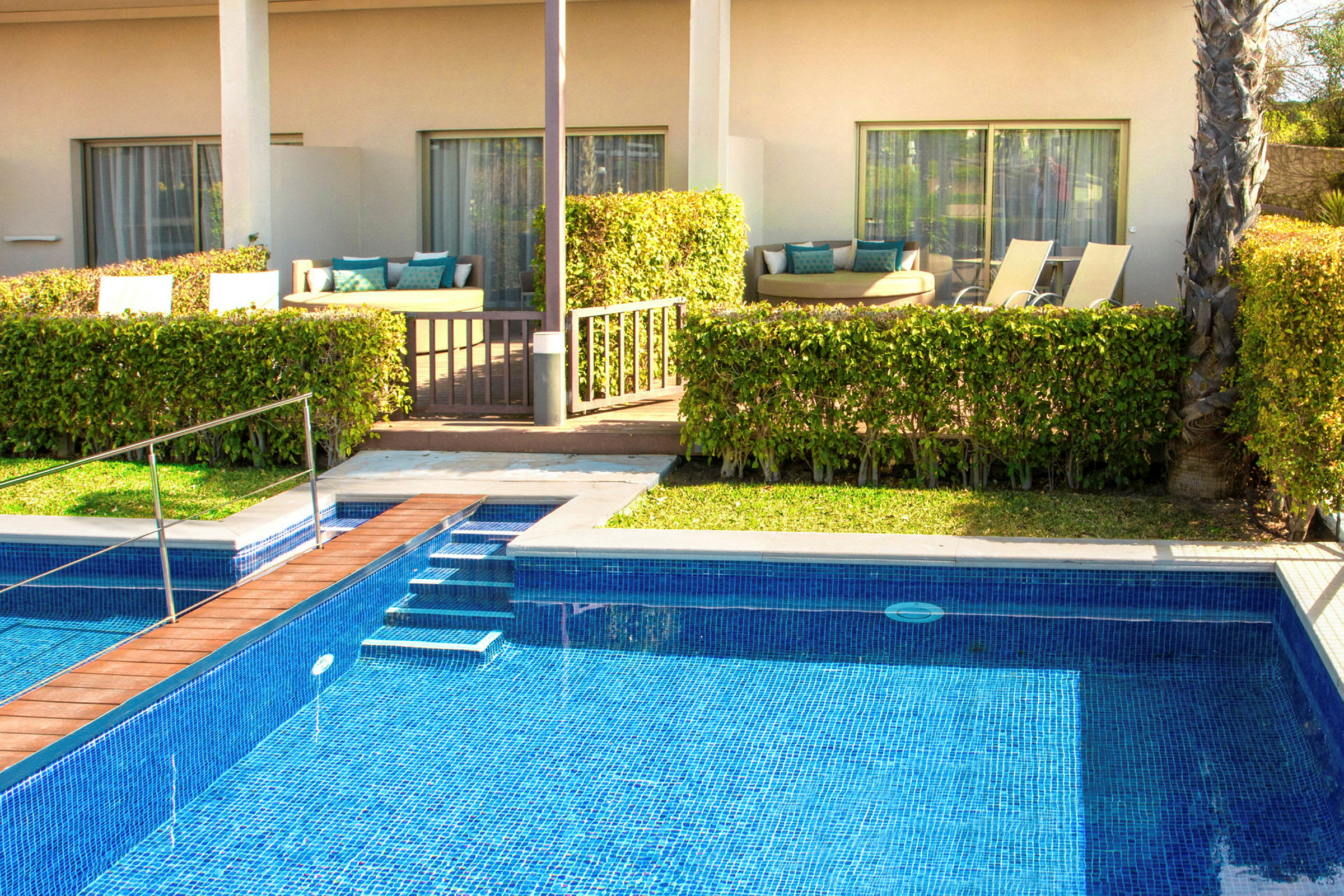 En pool framför en terrass med sittmöbler och solstolar. (AI-genererad text)