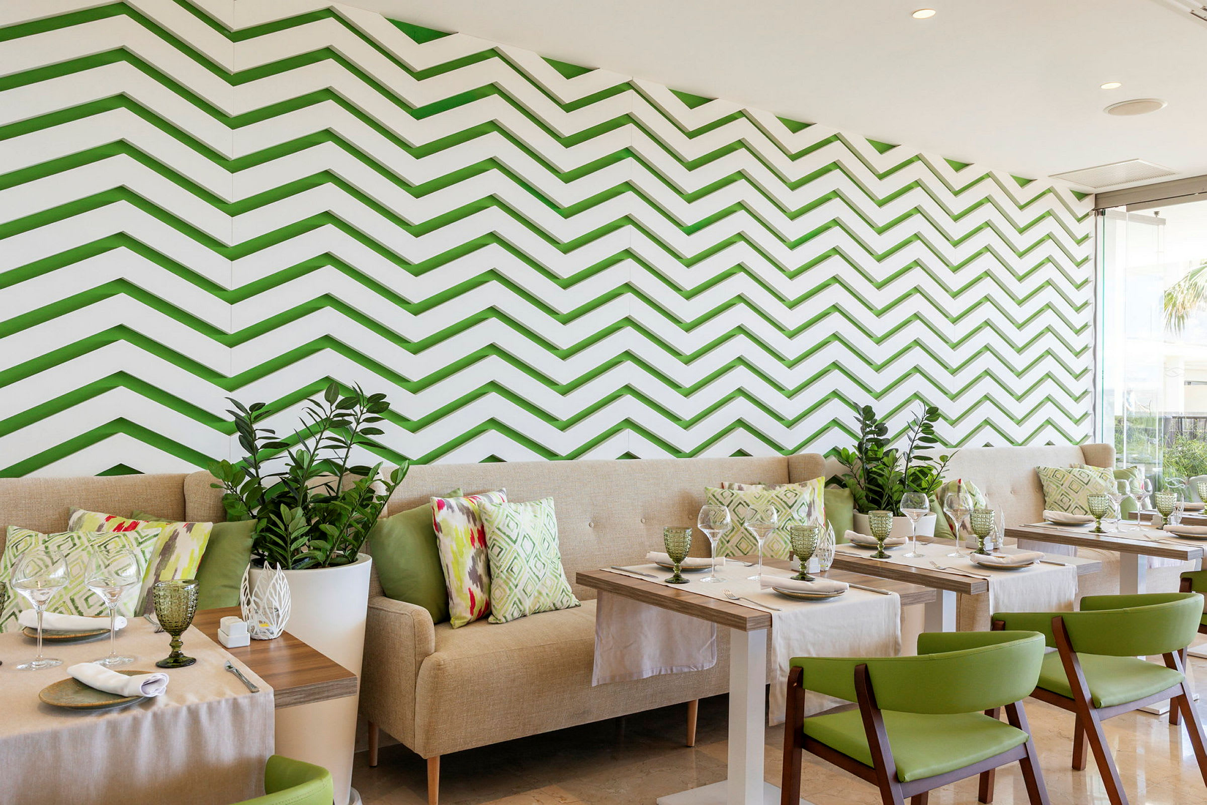 En restaurang med modern inredning, gröna stolar, ljusa soffor och en vägg med gröna sicksack-mönster. (AI-genererad text)