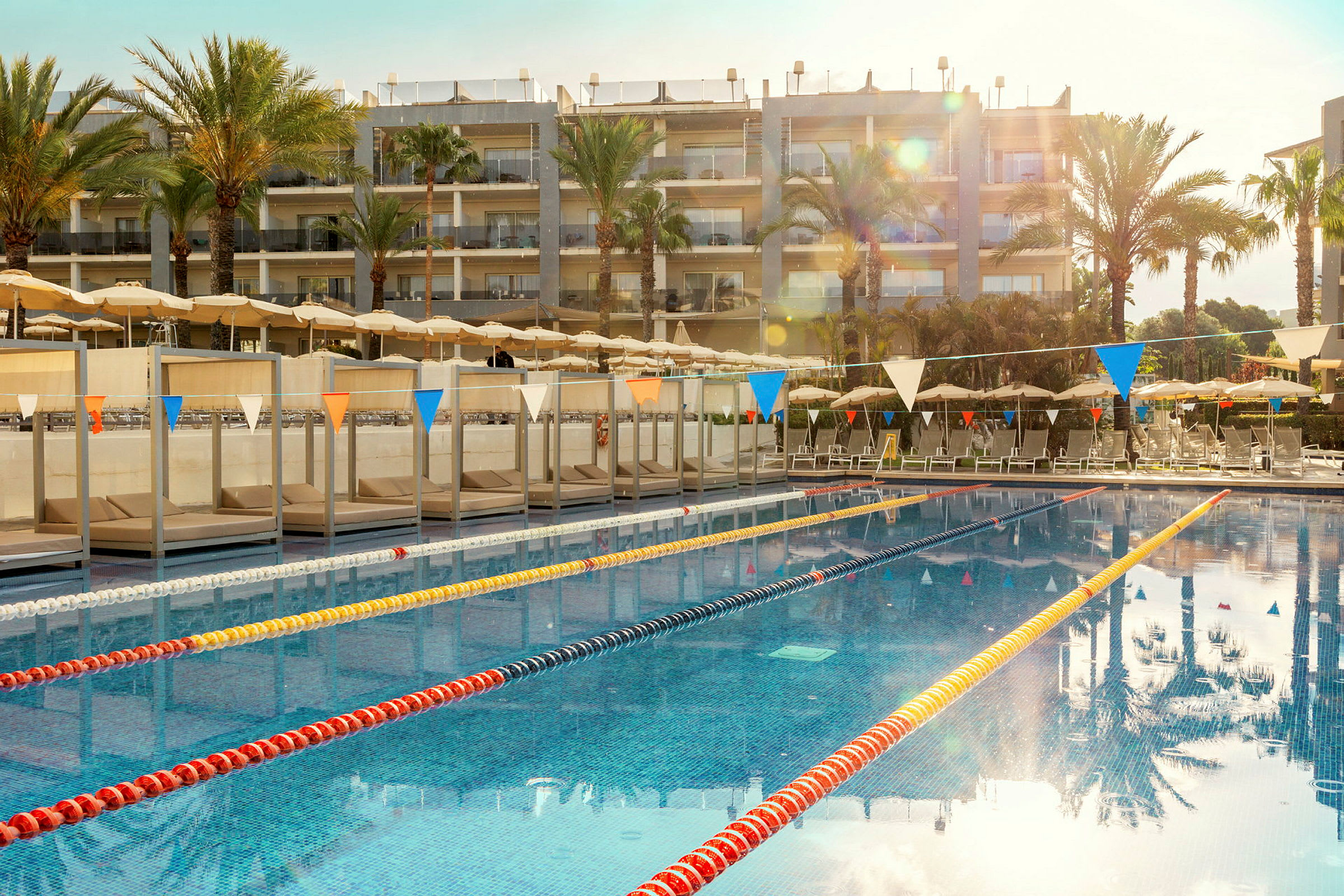 En swimmingpool vid ett hotell med solstolar och parasoller i bakgrunden. (AI-genererad text)