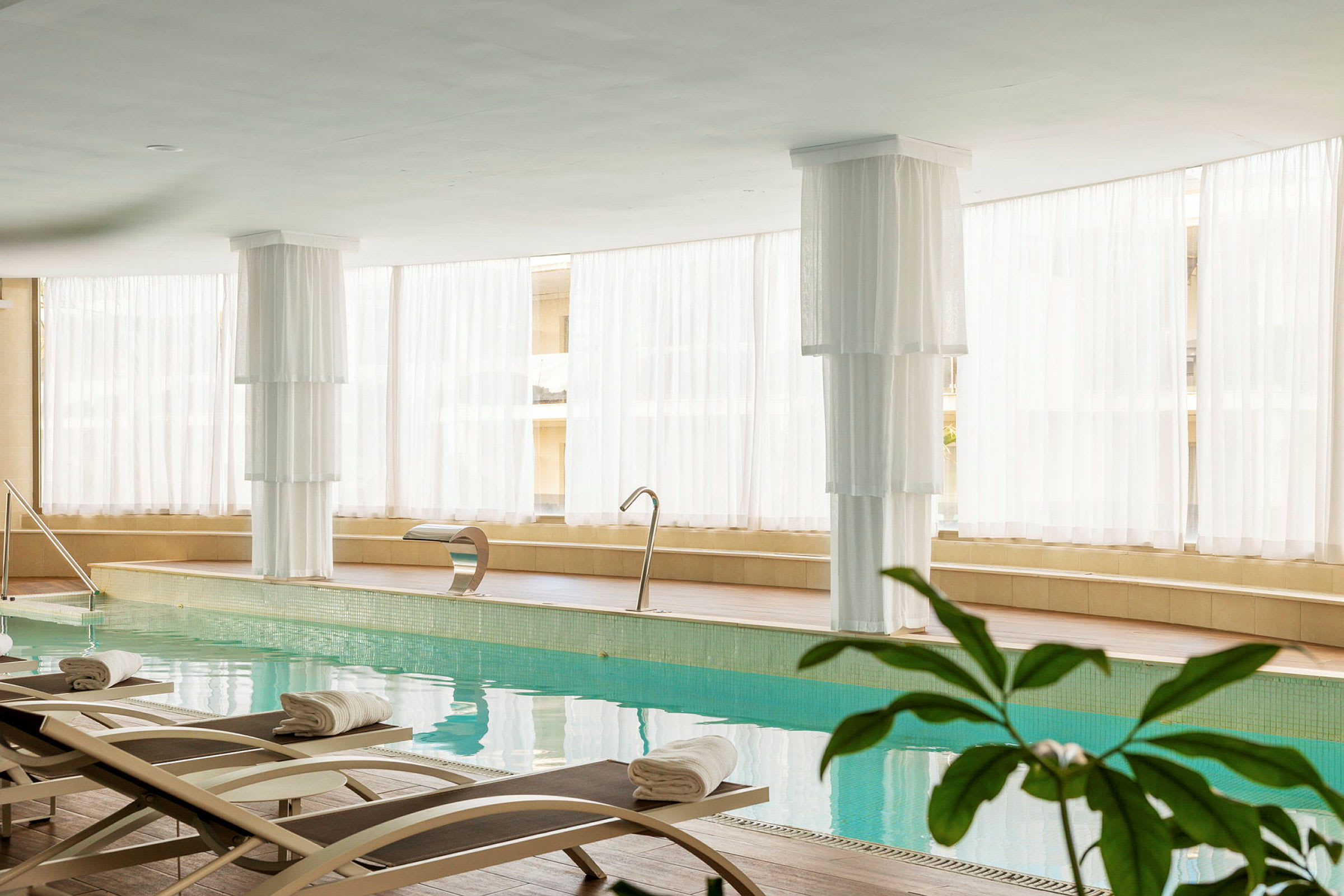 Interiör av ett ljust spa med inomhuspool, solstolar och vit inredning. (AI-genererad text)