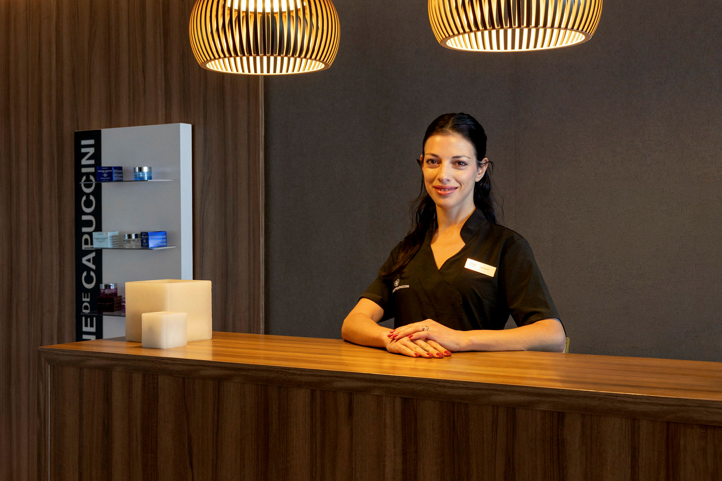 En kvinna i arbetskläder står bakom en receptionsdisk i en varm belysning. (AI-genererad text)