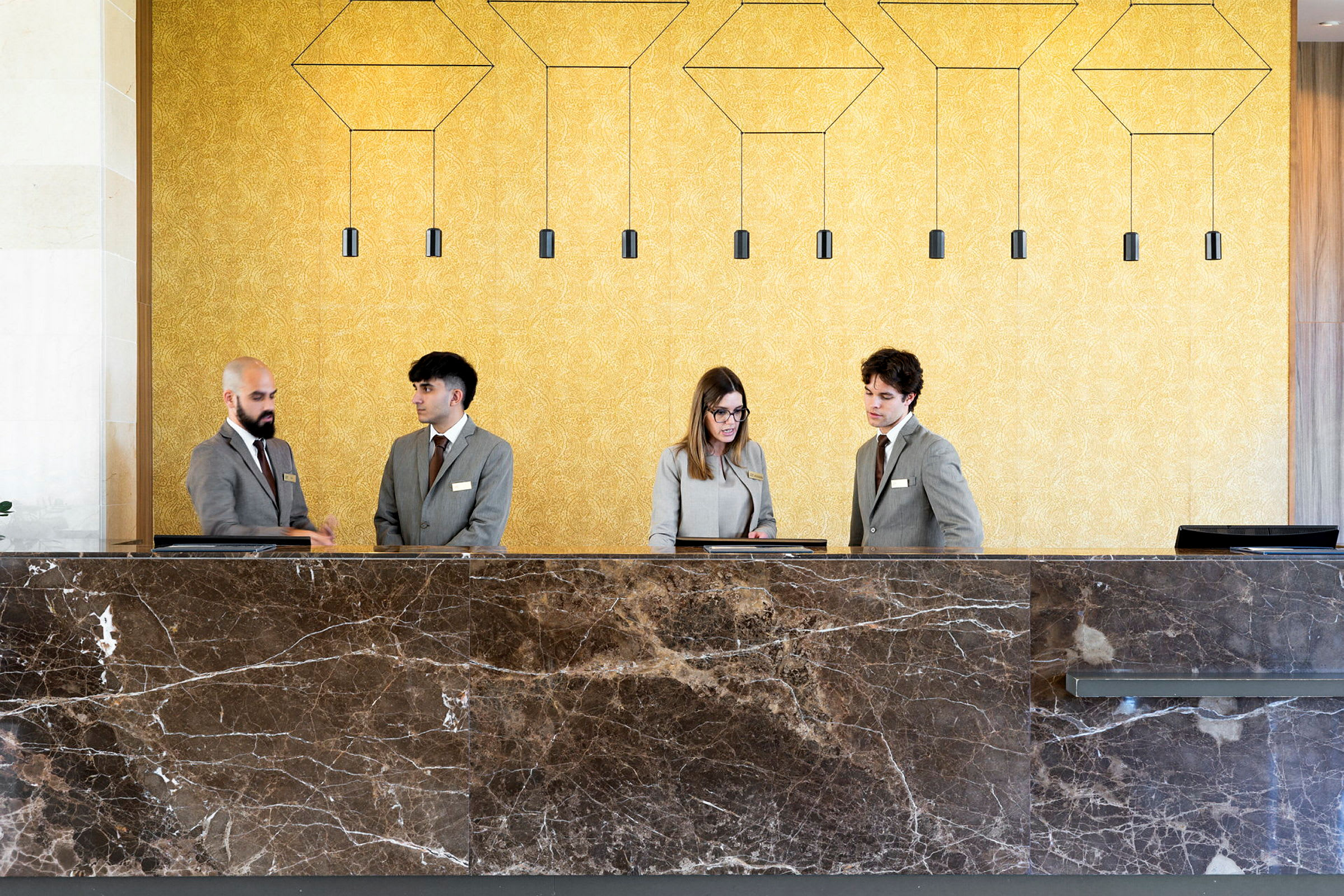 Personal i hotellreception iklädd uniformer vid en stor marmordisk. (AI-genererad text)
