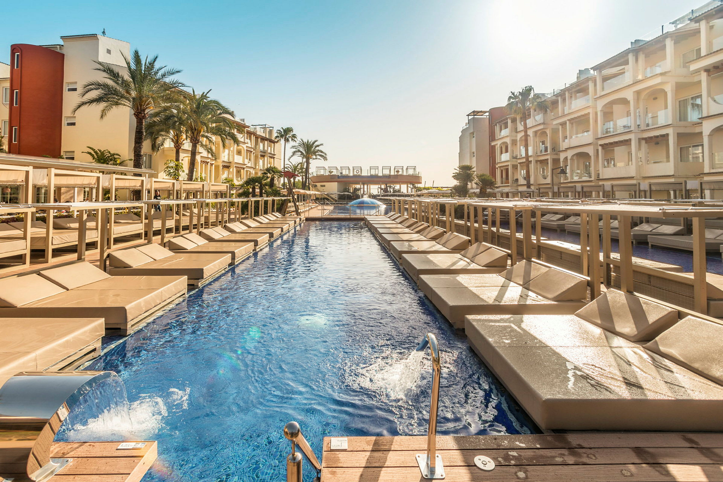 En swimmingpool omgiven av solstolar och byggnader. (AI-genererad text)