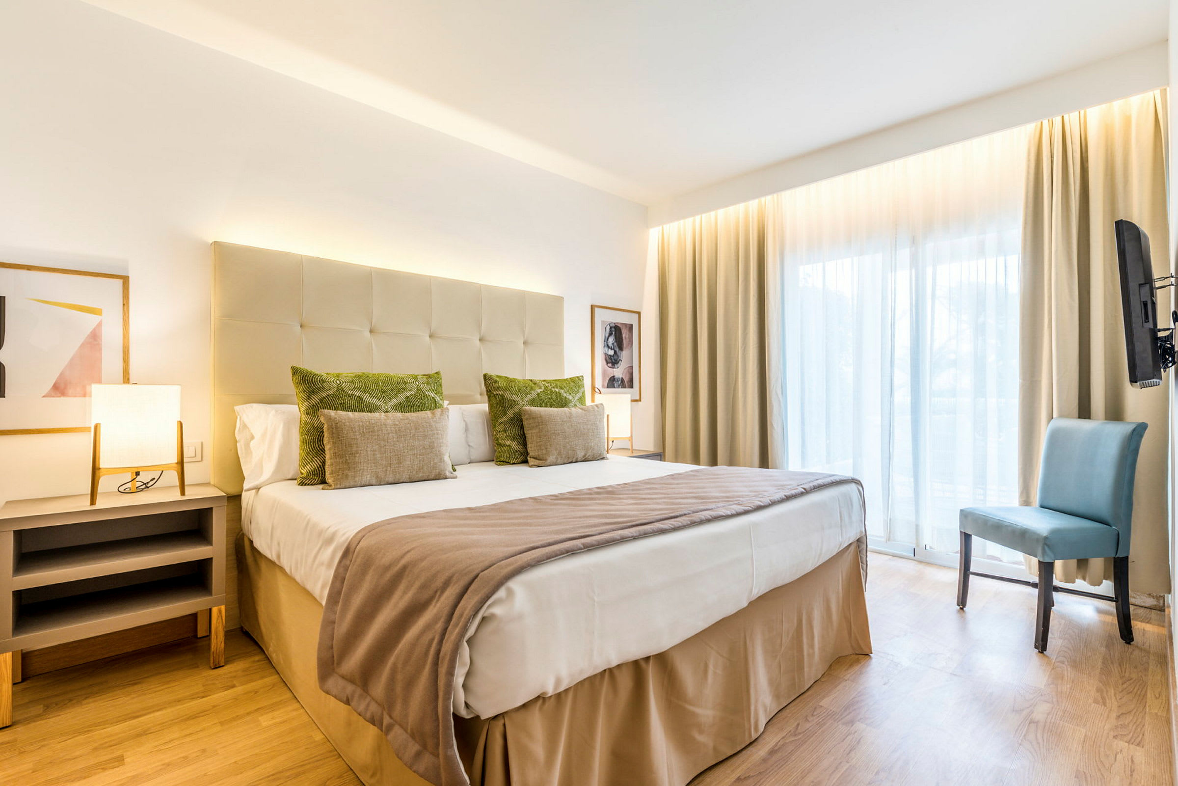 Ett hotellrum med en dubbelsäng, sidobord, stol och stort fönster. (AI-genererad text)