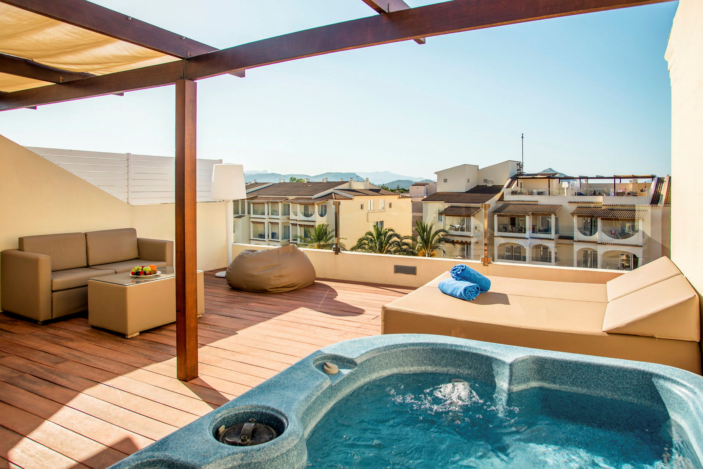 Terrass med bubbelpool, soffa och utsikt över omgivande byggnader. (AI-genererad text)