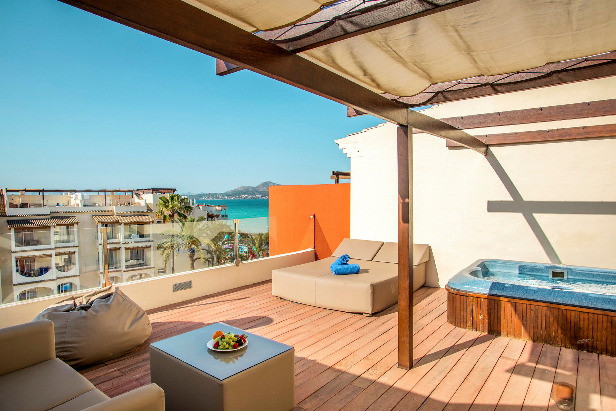 Takterrass med jacuzzi, solbädd och sittplatser, utsikt mot havet och byggnader. (AI-genererad text)