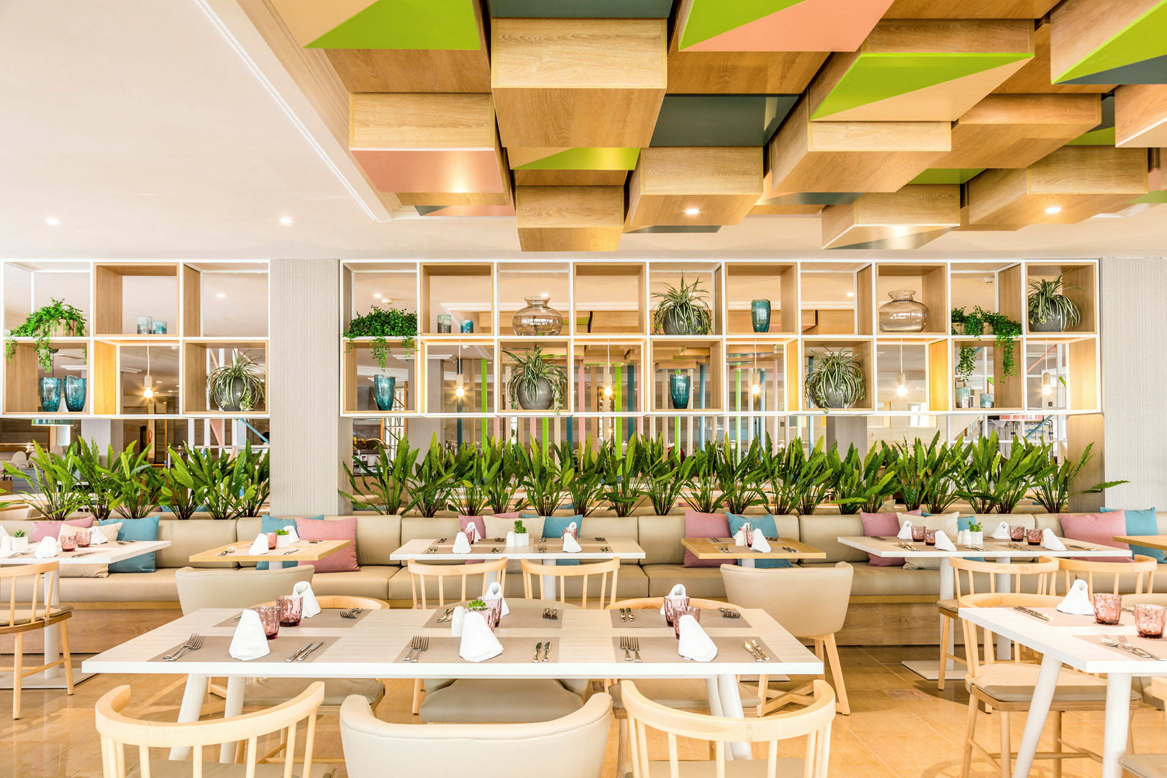 Modern restaurang med träbord, stolar och dekorationer som inkluderar växter och kuddar. (AI-genererad text)