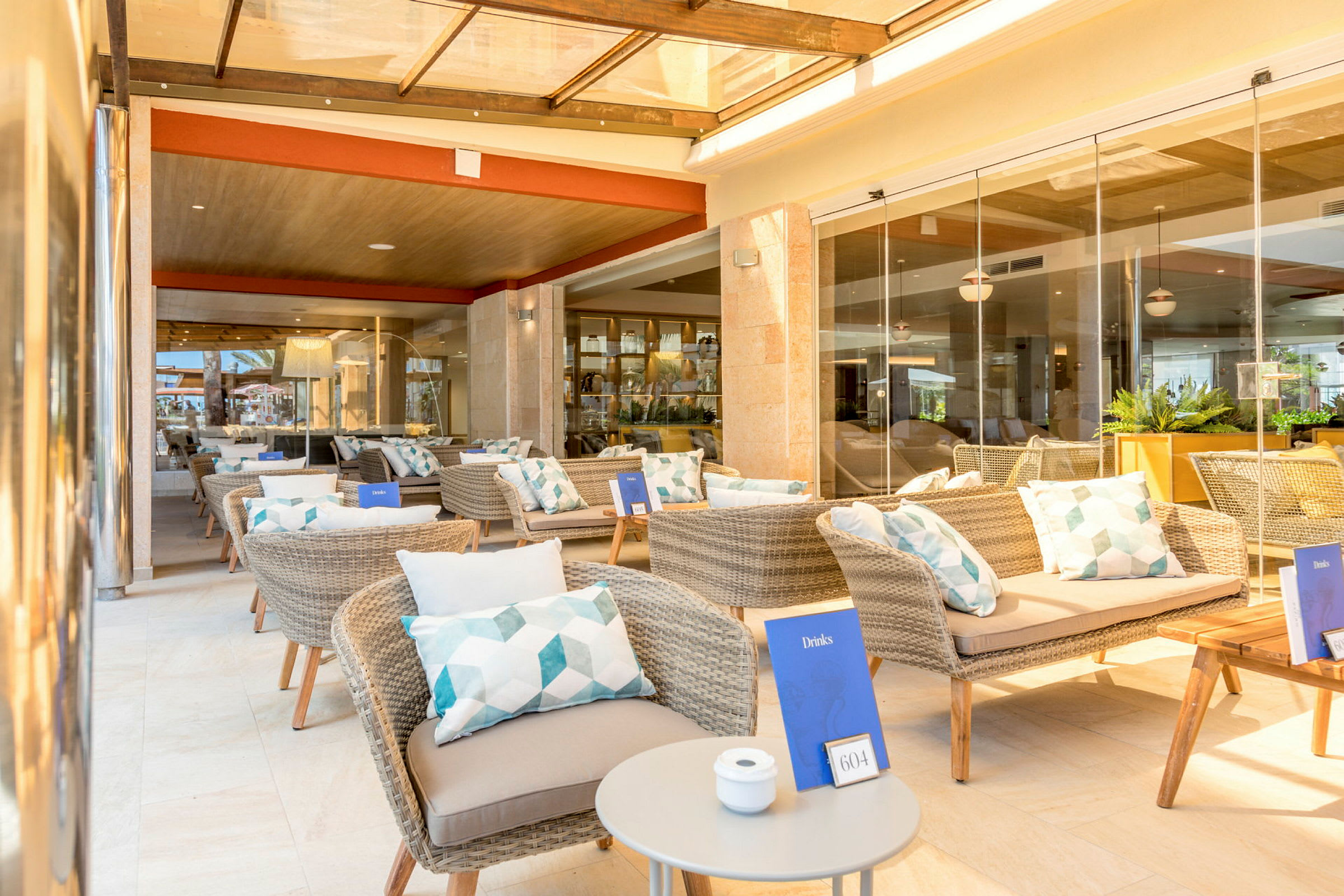 Loungeområde med flätade stolar och bord, dekorerat med kuddar och menyer. (AI-genererad text)