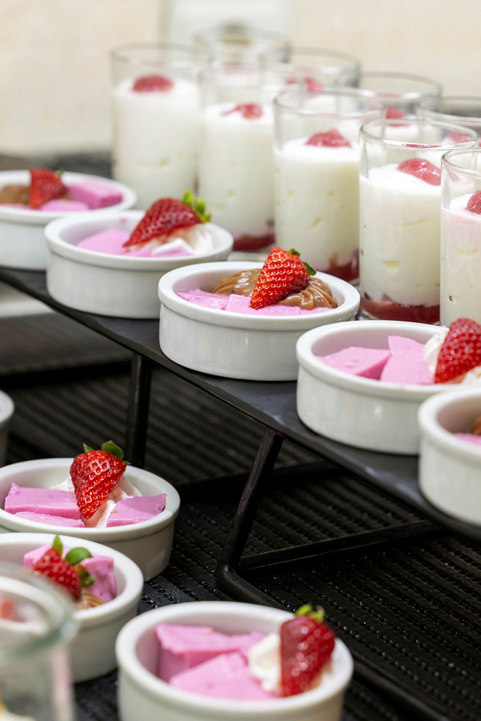 Ett urval av desserter, inklusive skålar med rosa mousse och jordgubbar samt glas med vit mousse och jordgubbar. (AI-genererad text)