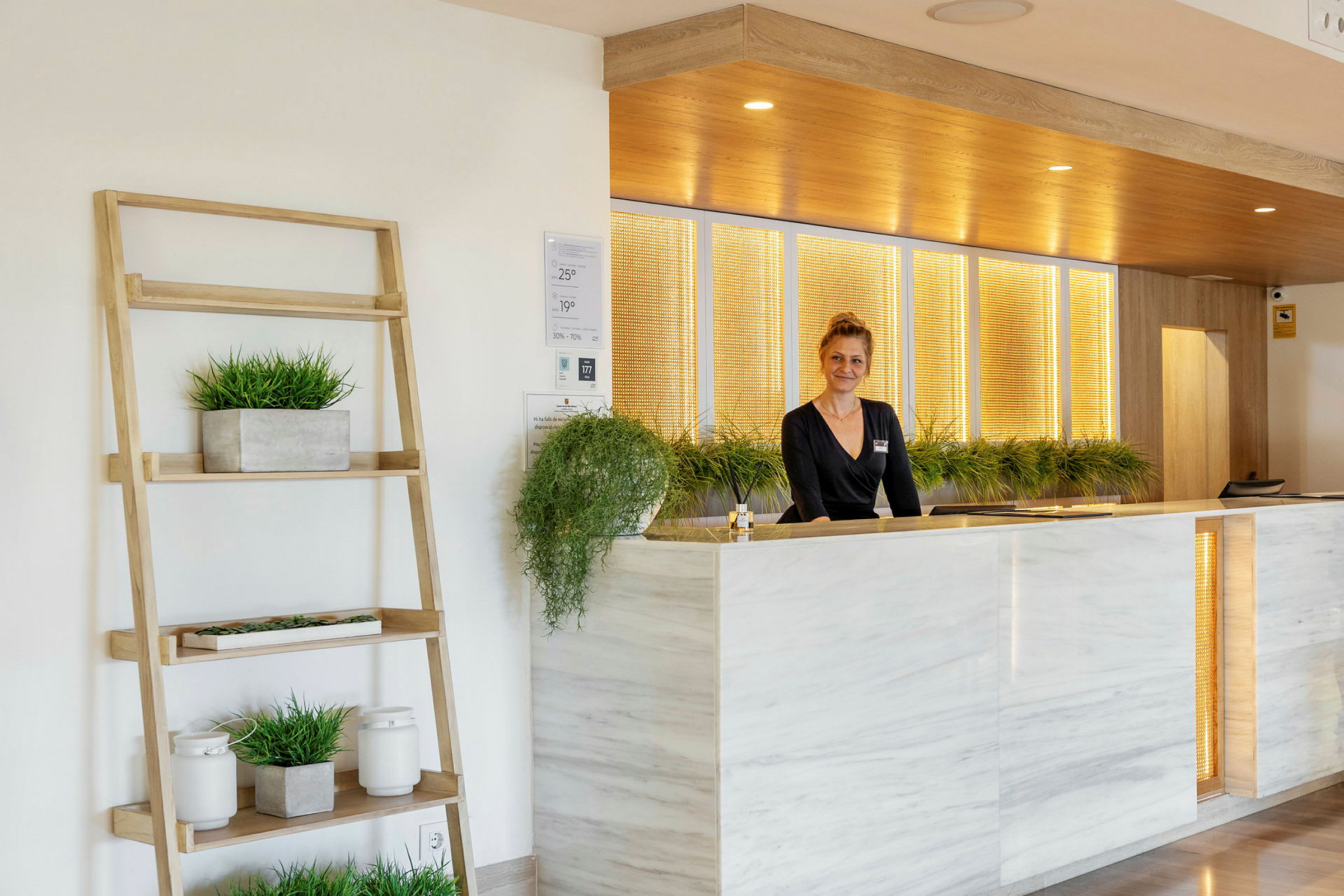 Reception med marmorpanel och växter. En person står bakom disken. (AI-genererad text)