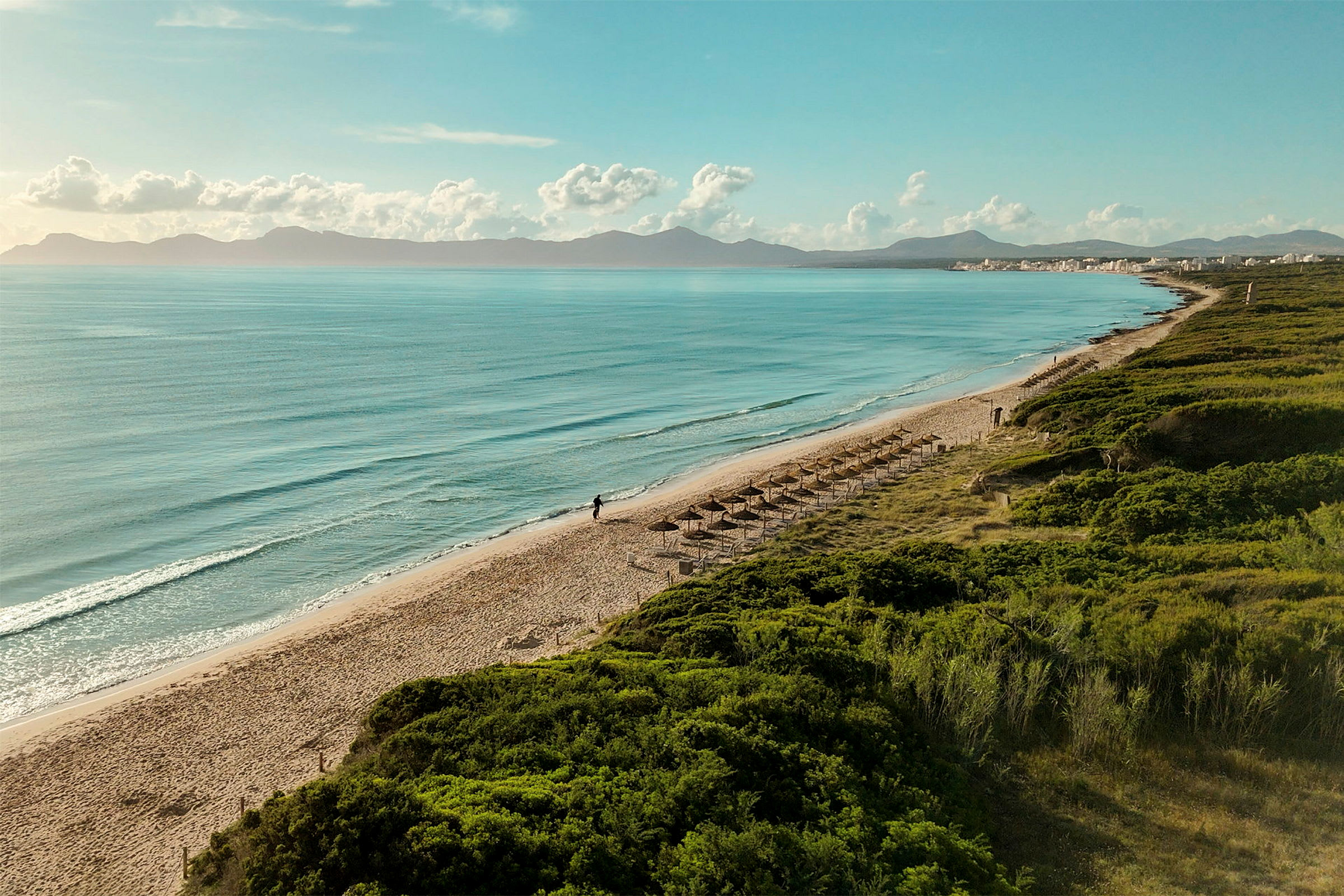 Strand med parasoller, hav och berg i bakgrunden. (AI-genererad text)