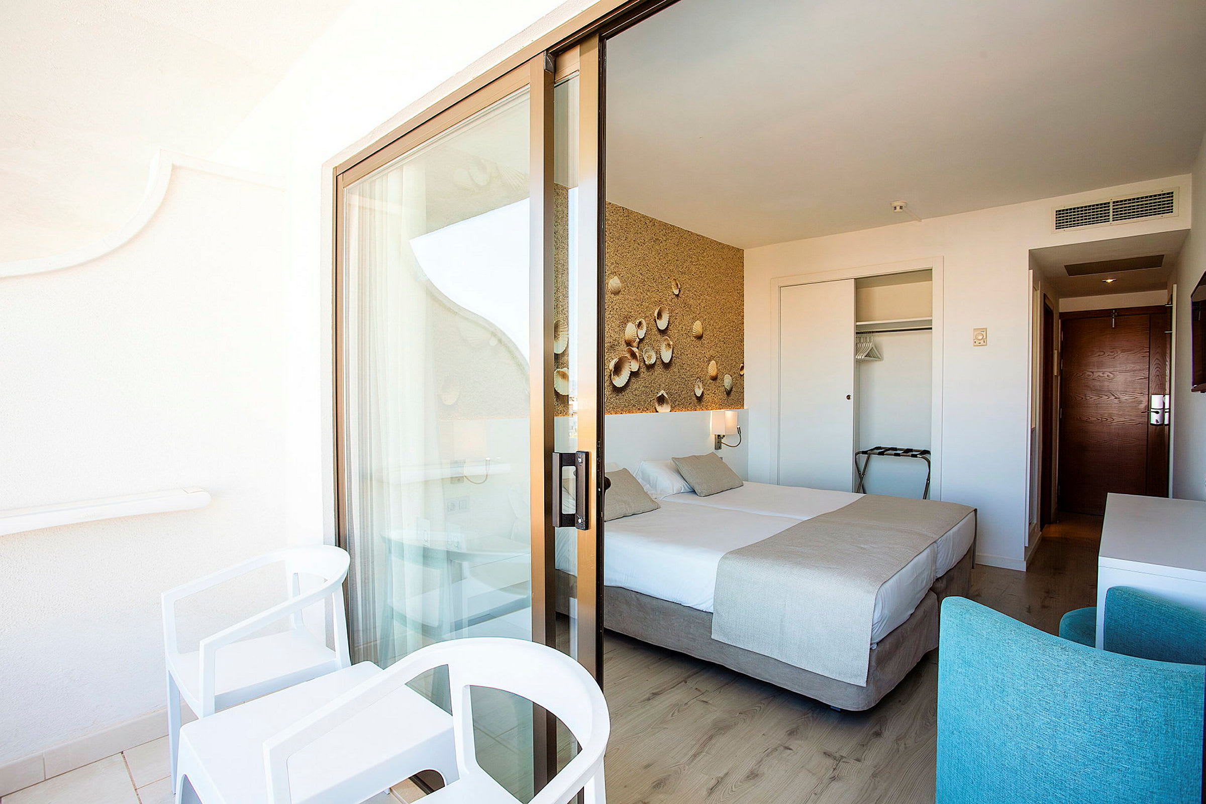 Hotellrum med balkong, dubbelsäng och inredning i ljusa toner. (AI-genererad text)