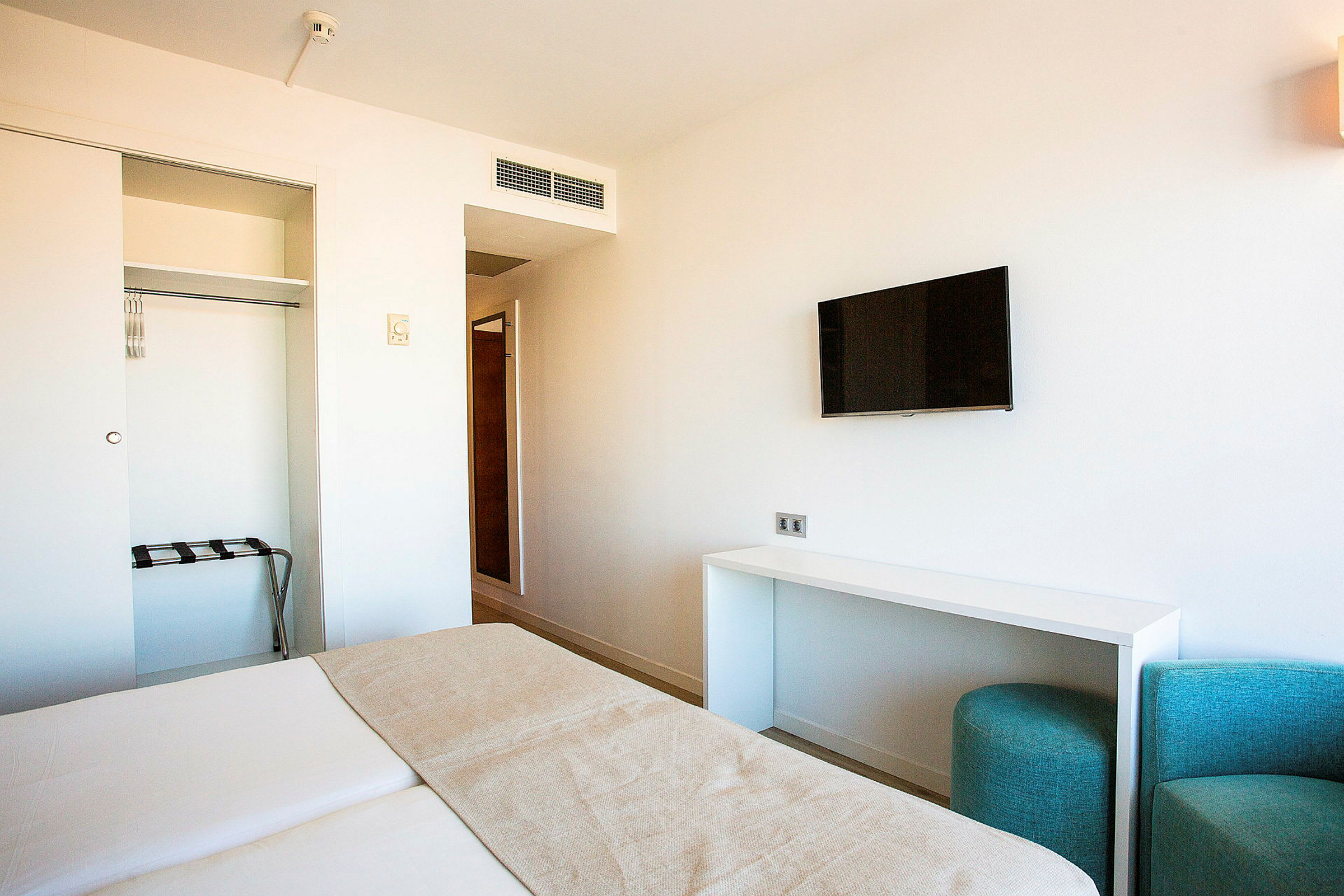 Ett modernt hotellrum med en säng, en väggmonterad TV, och en öppen garderob. (AI-genererad text)