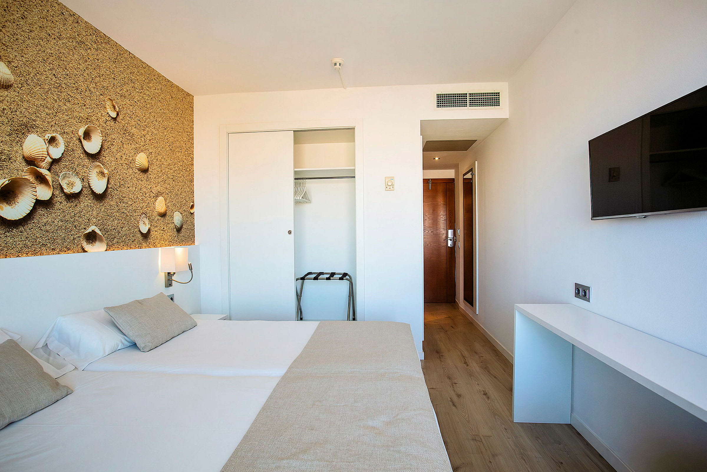 Ett hotellrum med en säng, väggdekoration med snäckmotiv, garderob och en TV. (AI-genererad text)
