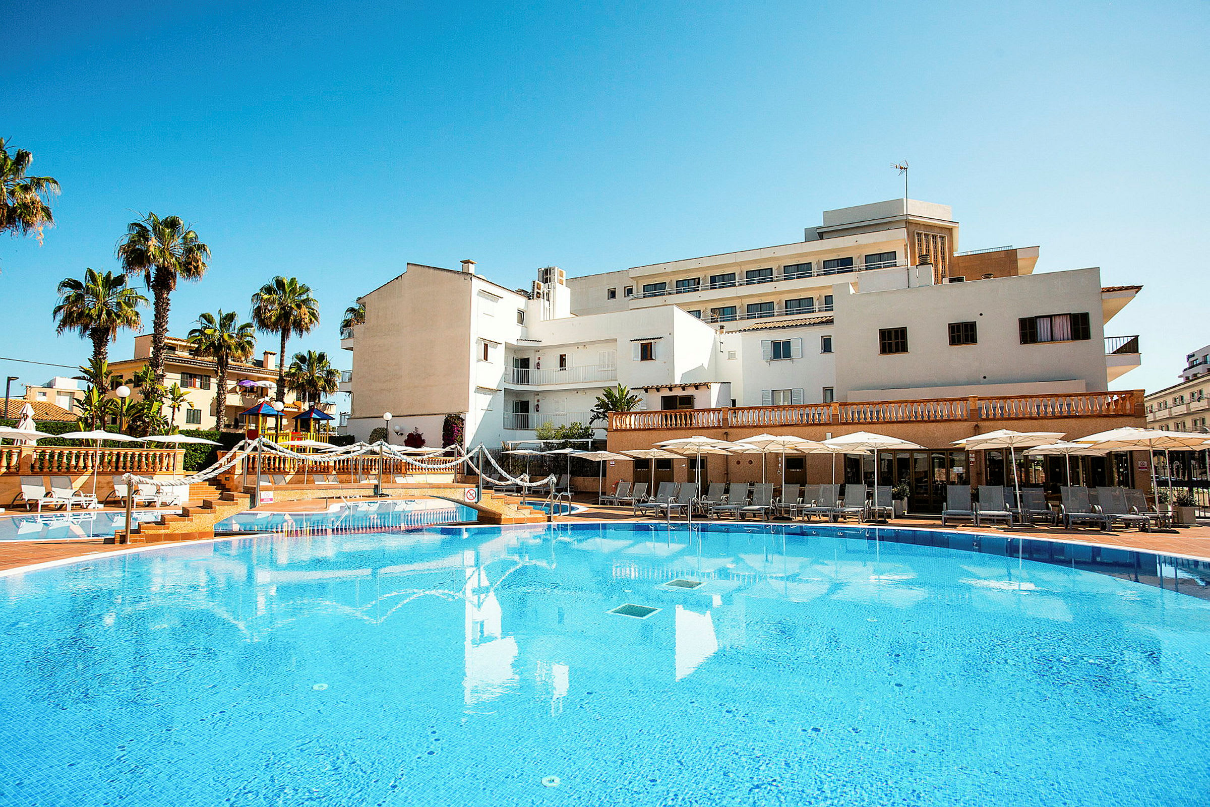 Bild av hotell med pool, solstolar och parasoller, med palmer i bakgrunden. (AI-genererad text)