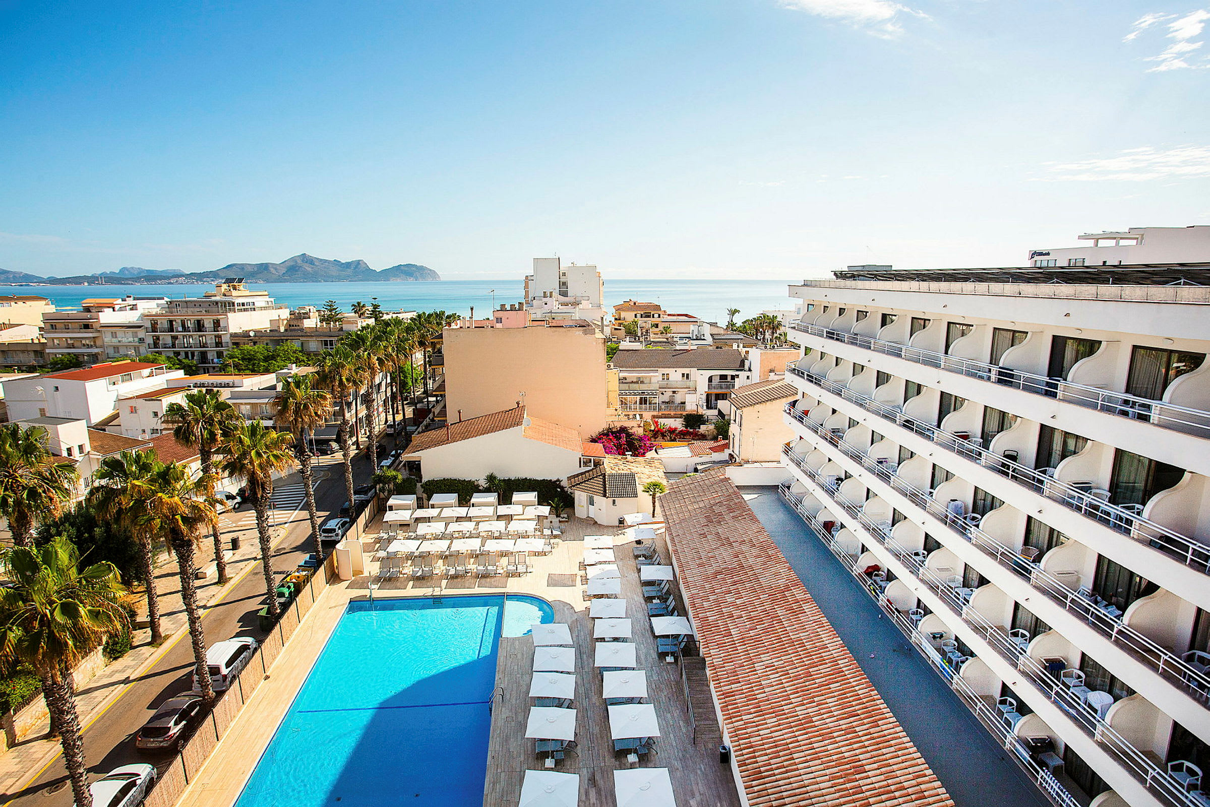 Vy från ovan över en hotellbyggnad, pool och omgivande område, med havet i bakgrunden. (AI-genererad text)