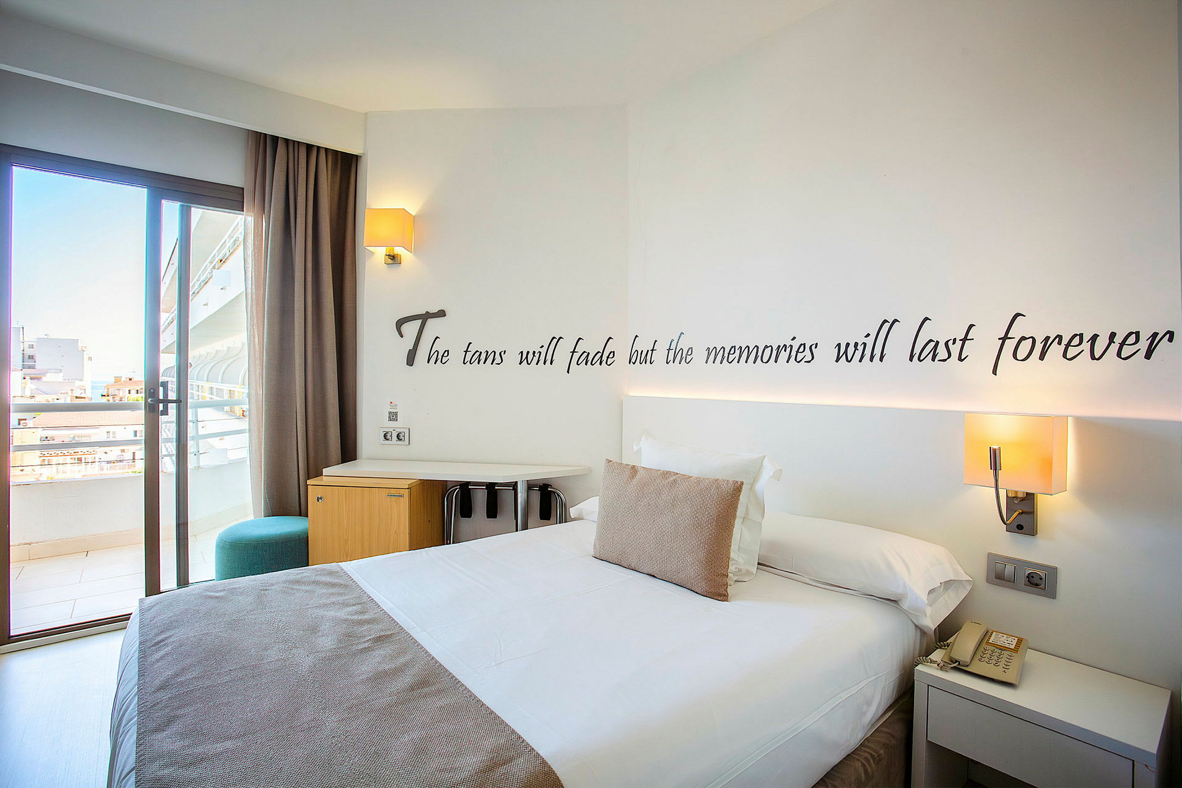 Hotellrum med en dubbelsäng, skrivbord och balkongdörr. (AI-genererad text)