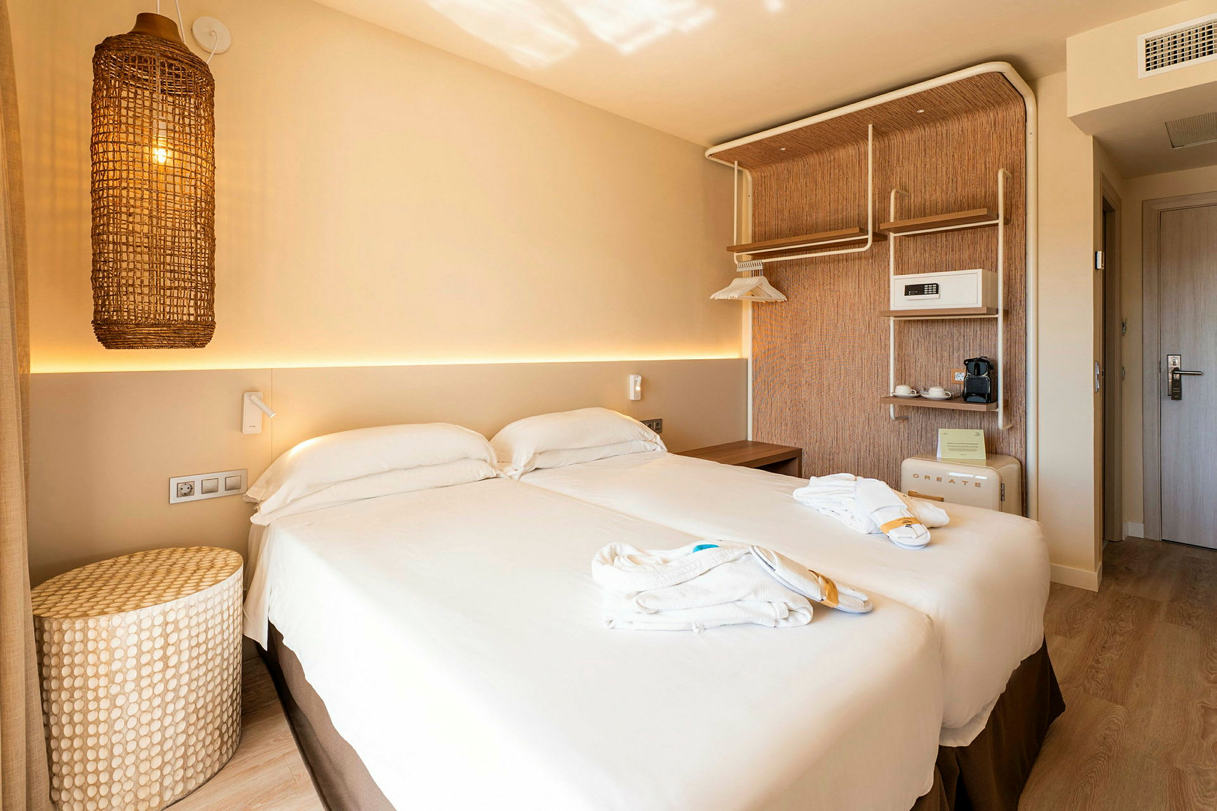 Ett hotellrum med en dubbelsäng, ljus inredning och en flätad lampa hängande på väggen. (AI-genererad text)