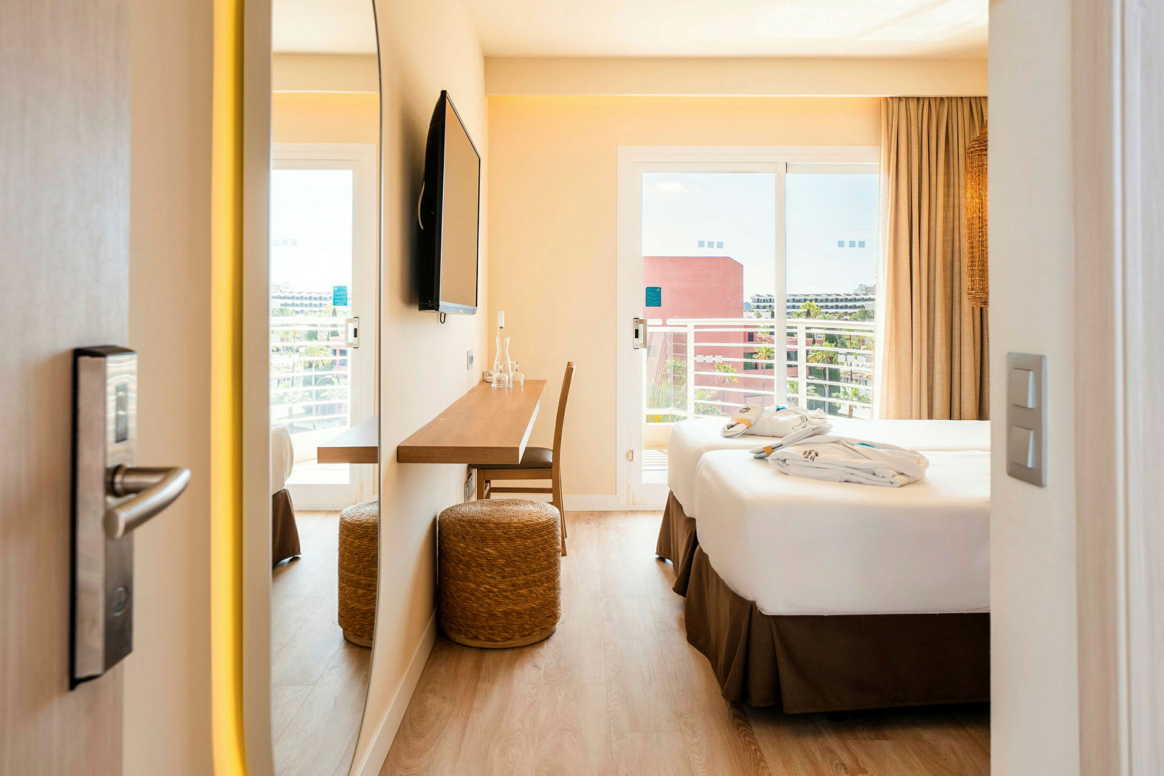 Ett hotellrum med en dubbelsäng, skrivbord och TV. Balkong med utsikt syns genom glasdörrarna. (AI-genererad text)