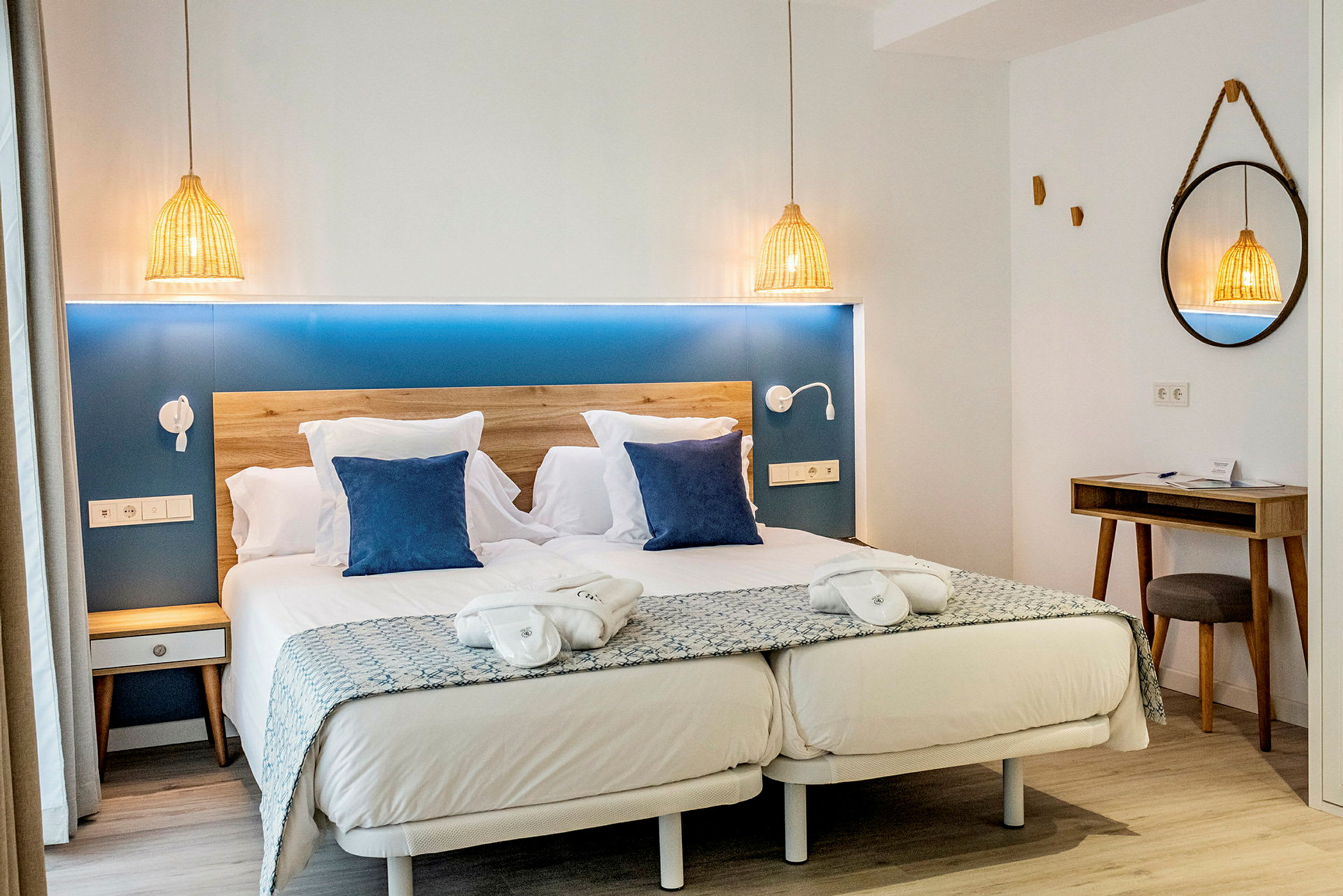 Ett hotellrum med en dubbelsäng, två blå kuddar, nattduksbord och en spegel. (AI-genererad text)