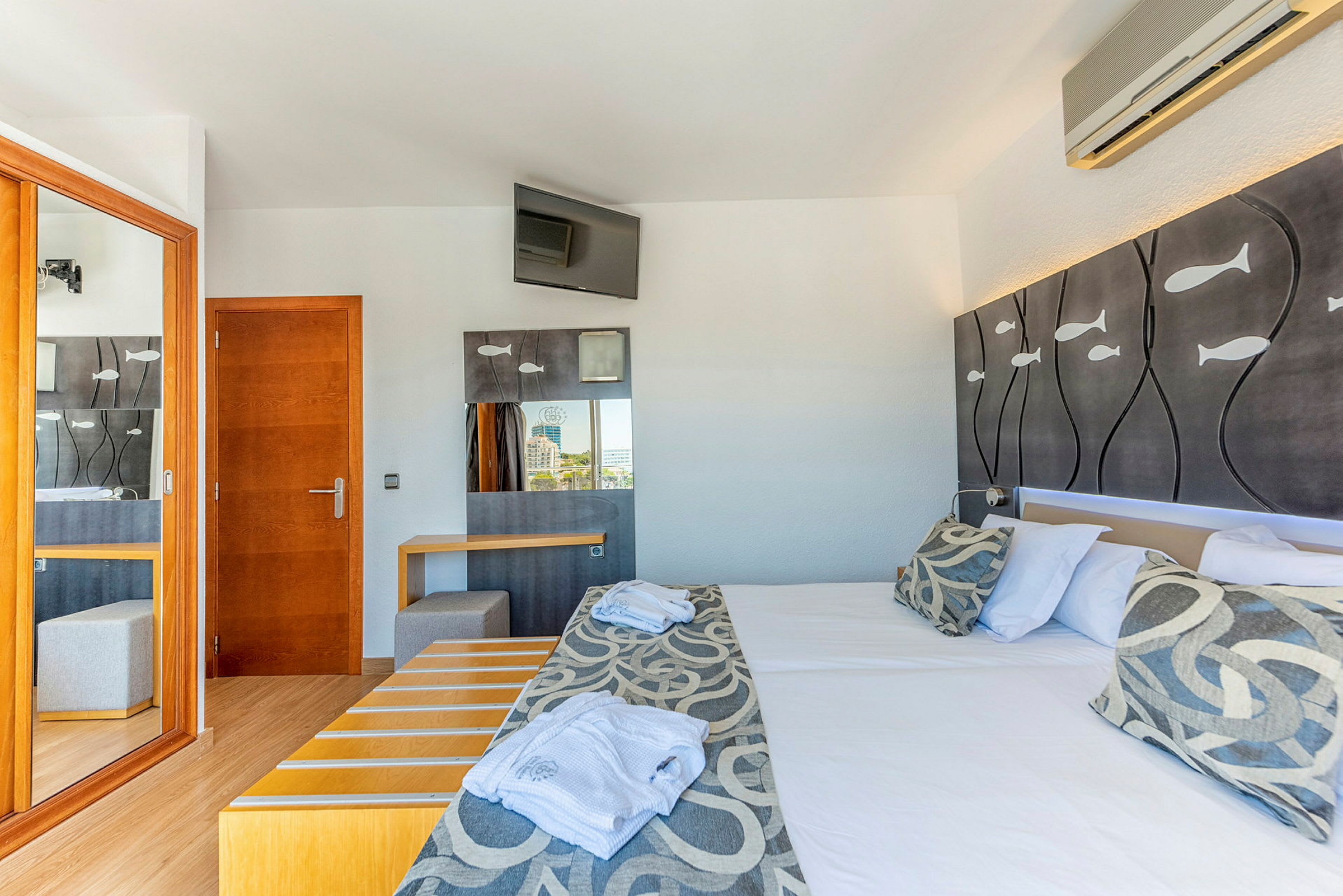 Ett hotellrum med en dubbelsäng, dekorerade prydnadsfiskar på huvudgaveln och ett skrivbord med en spegel. (AI-genererad text)